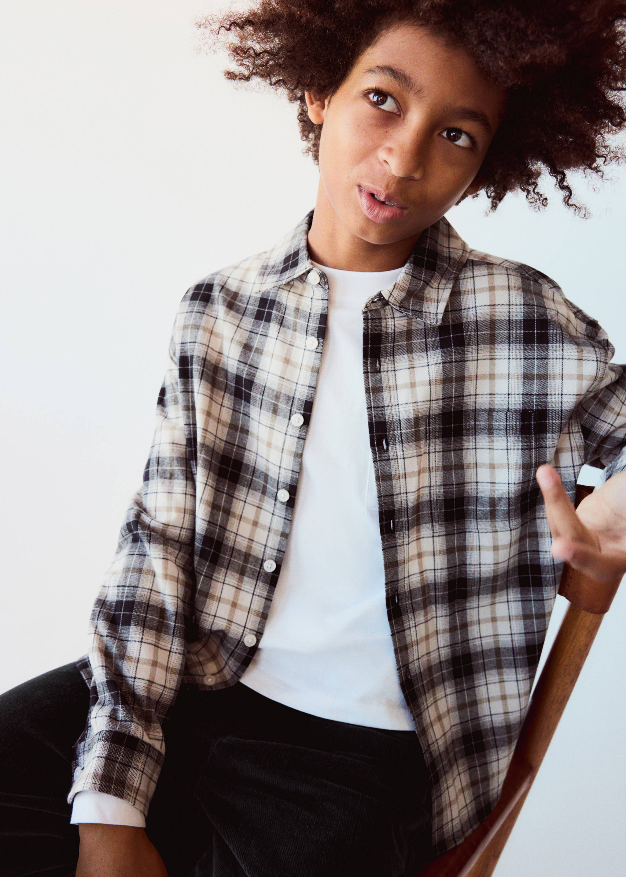Black, white, and beige plaid shirt worn open over a white t-shirt.