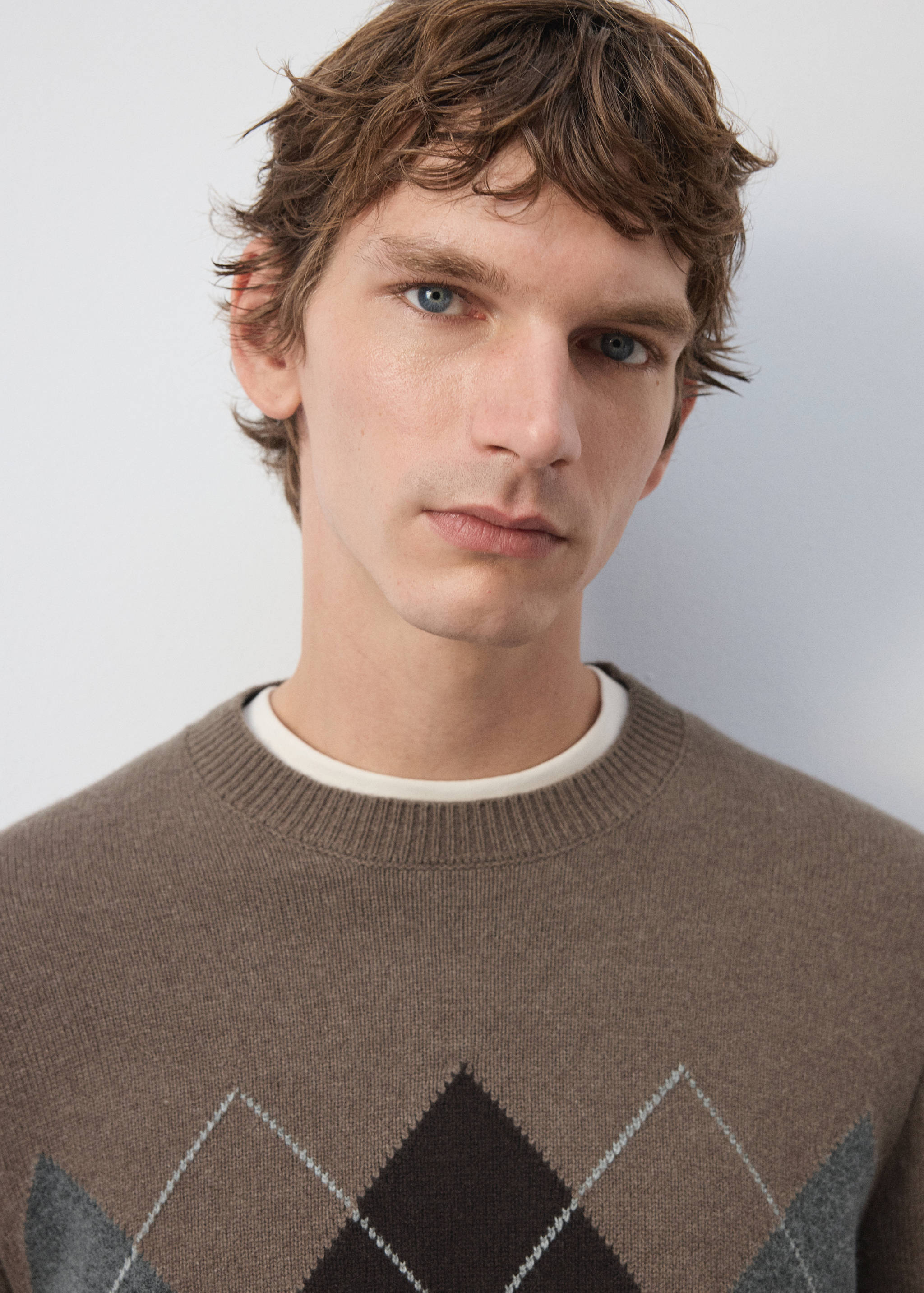 Brown crewneck sweater with an argyle pattern, worn with a layered t-shirt.