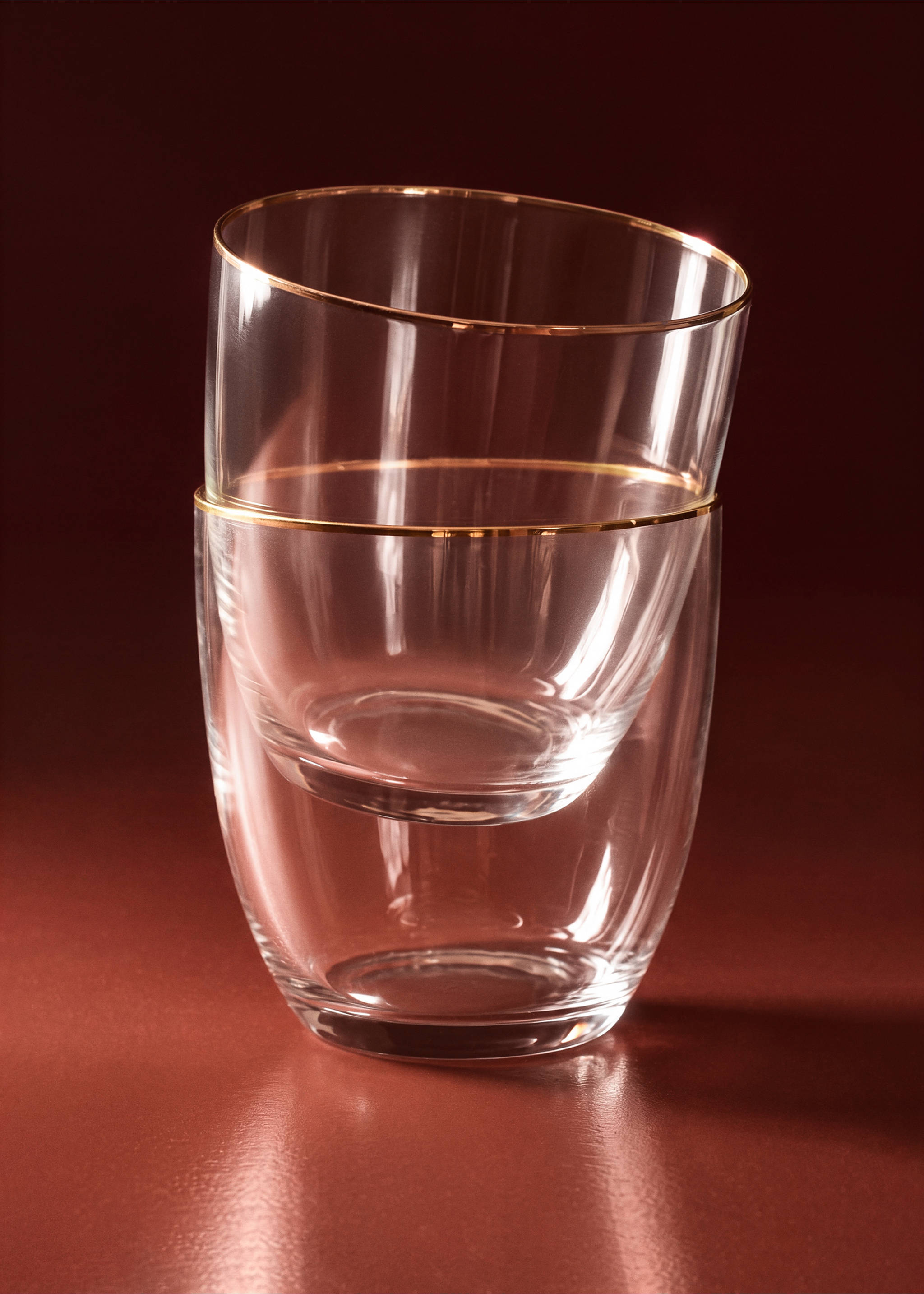 Two clear glass tumblers with gold rims, stacked creatively on a dark surface., Gold. Ref: 37067919-00.