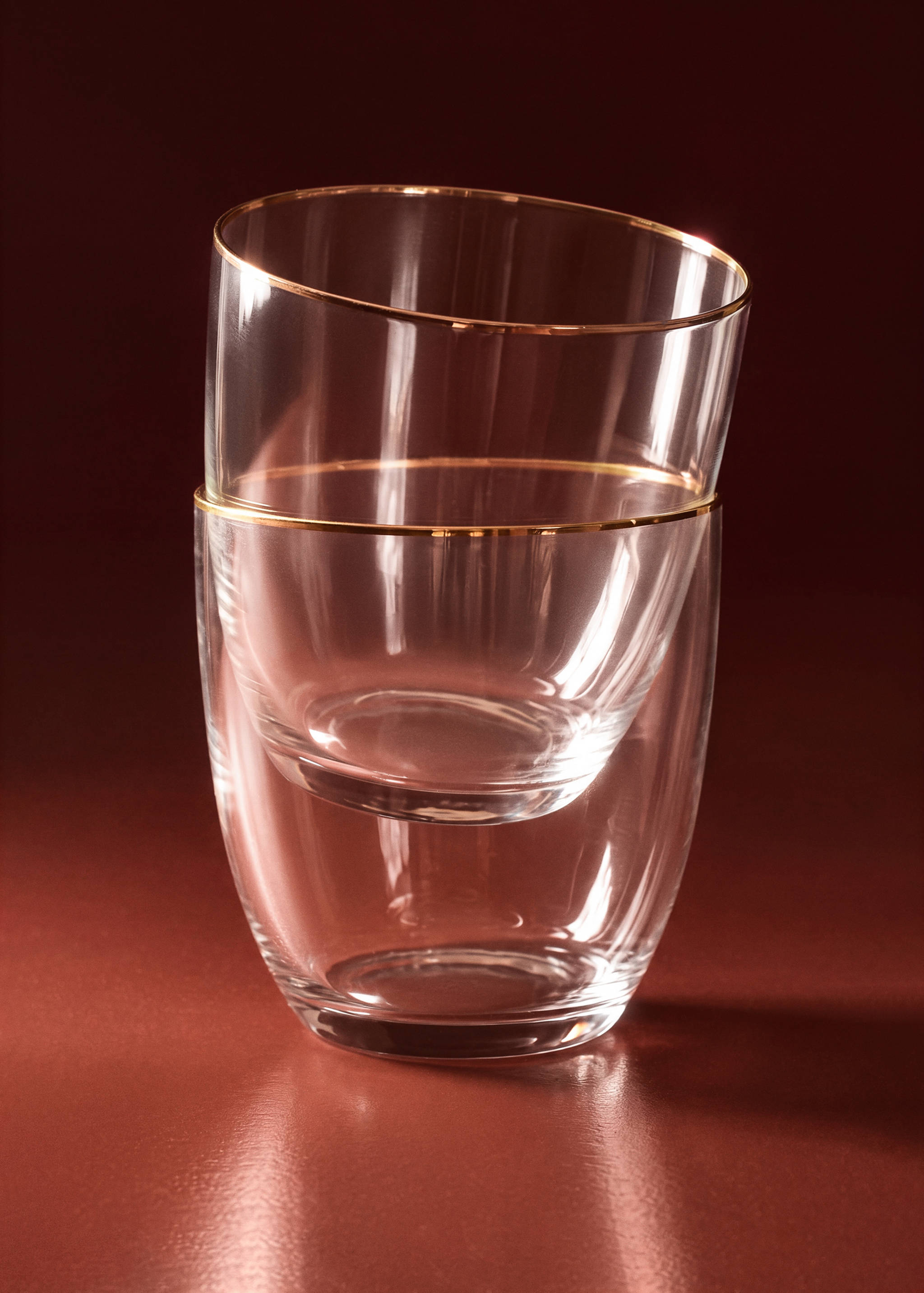 Two clear glass tumblers with gold rims, stacked creatively on a dark surface.