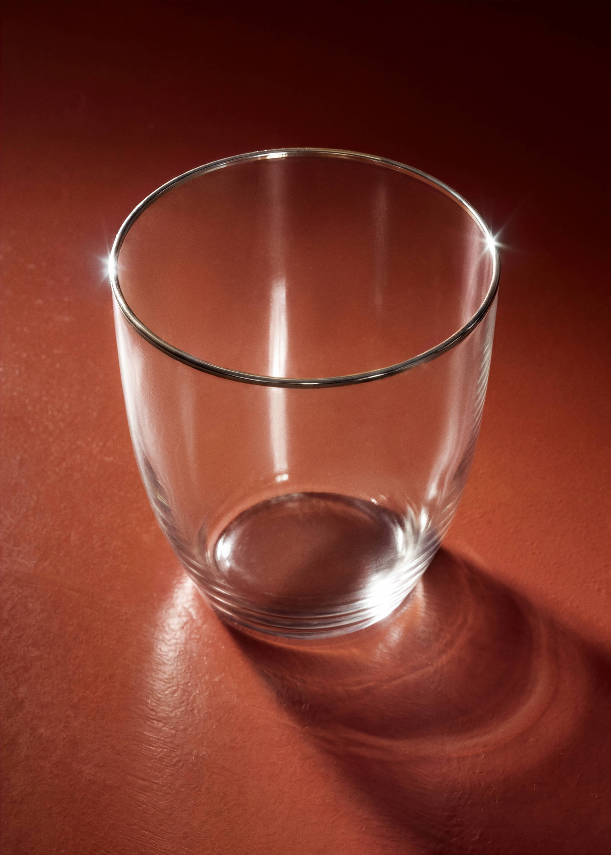 Clear glass tumbler with a metallic silver rim on a red surface.