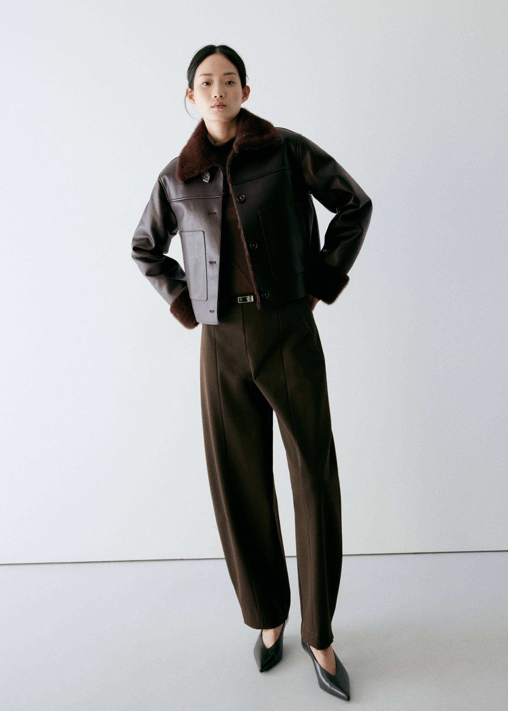 Dark brown jacket with plush faux-fur collar, paired with a dark top and matching trousers.
