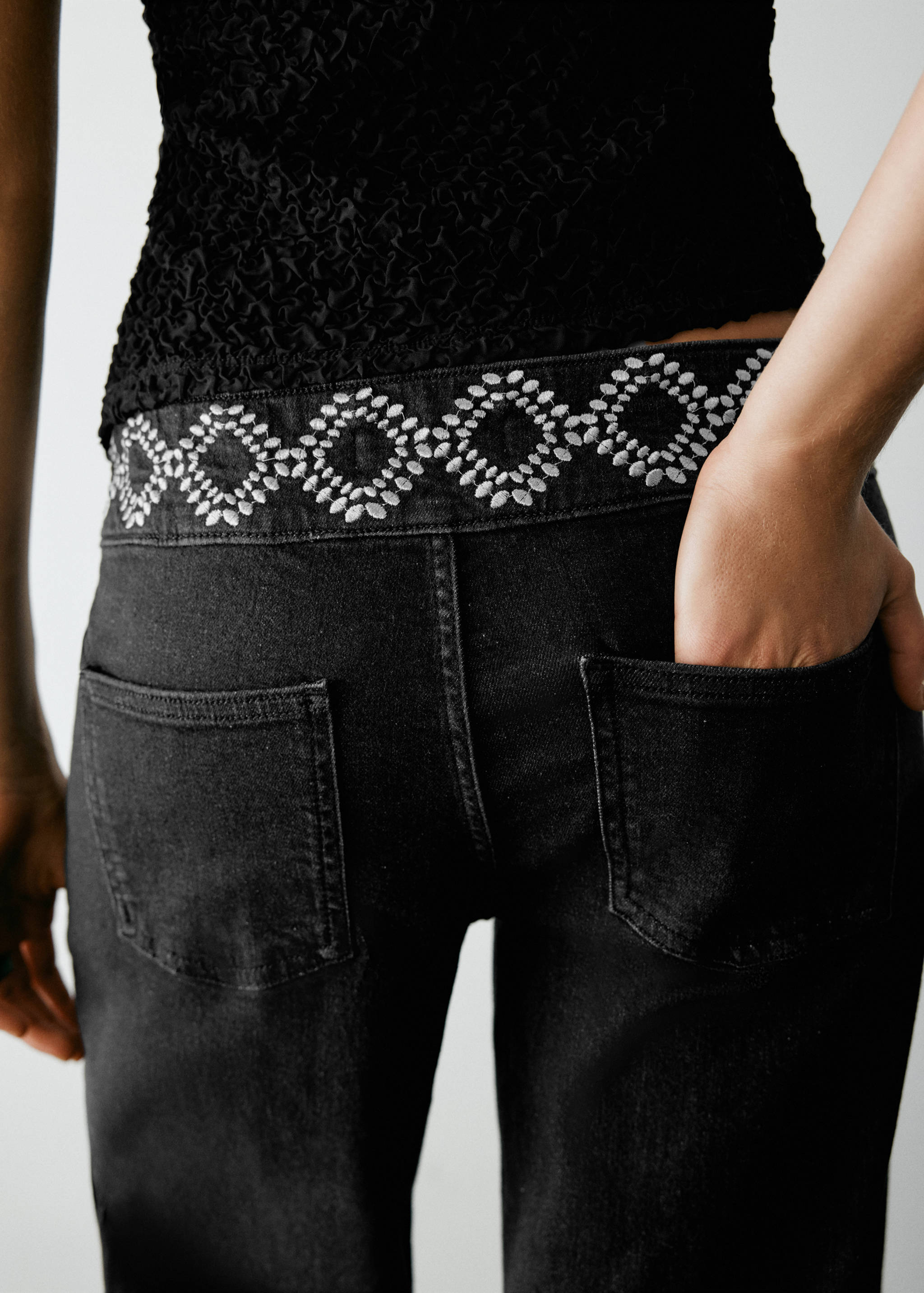 Close-up of black denim trousers with a geometric embroidered waistband.