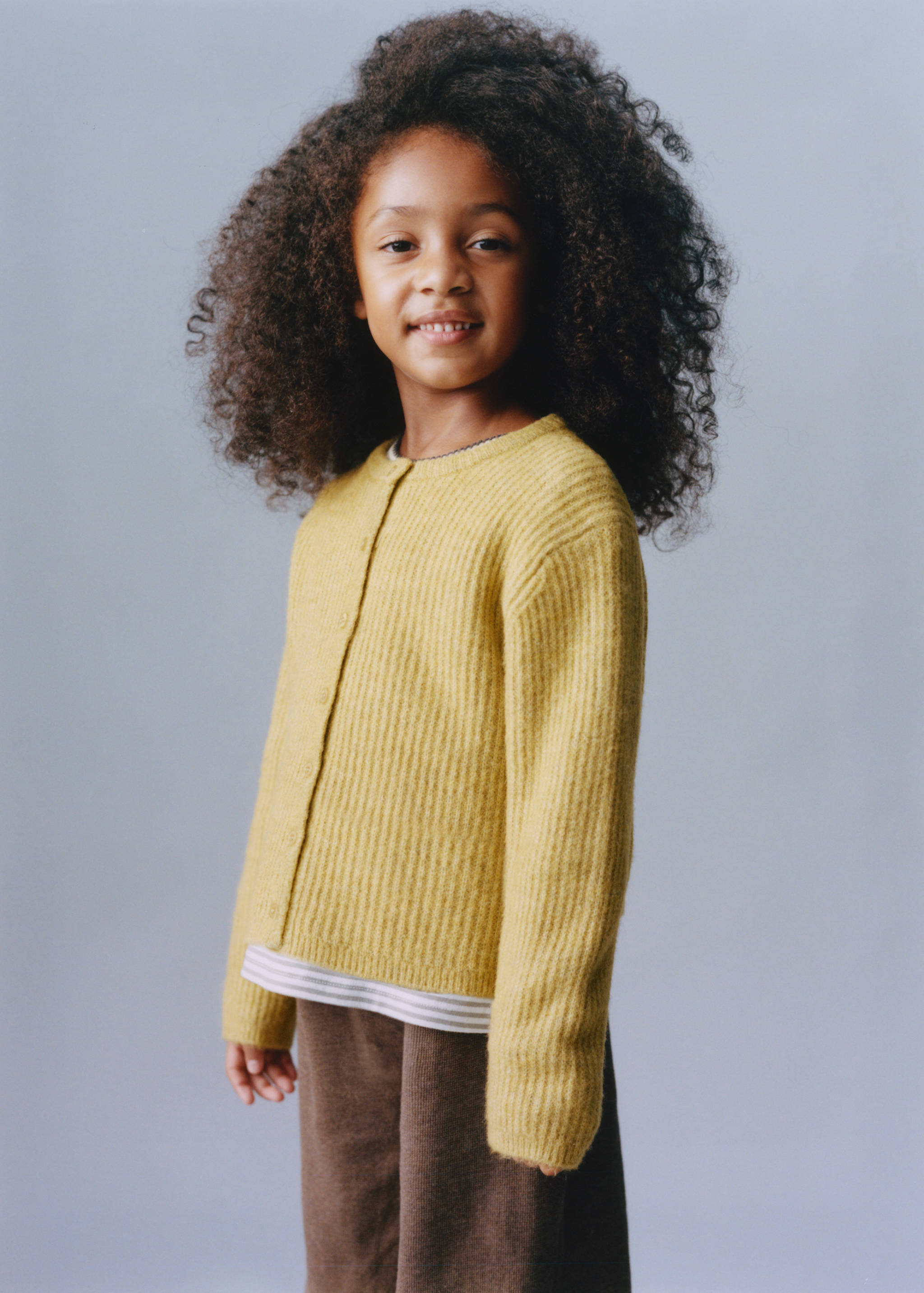 Mustard-yellow ribbed knit cardigan with a rounded neckline and front button fastening worn over a striped top.