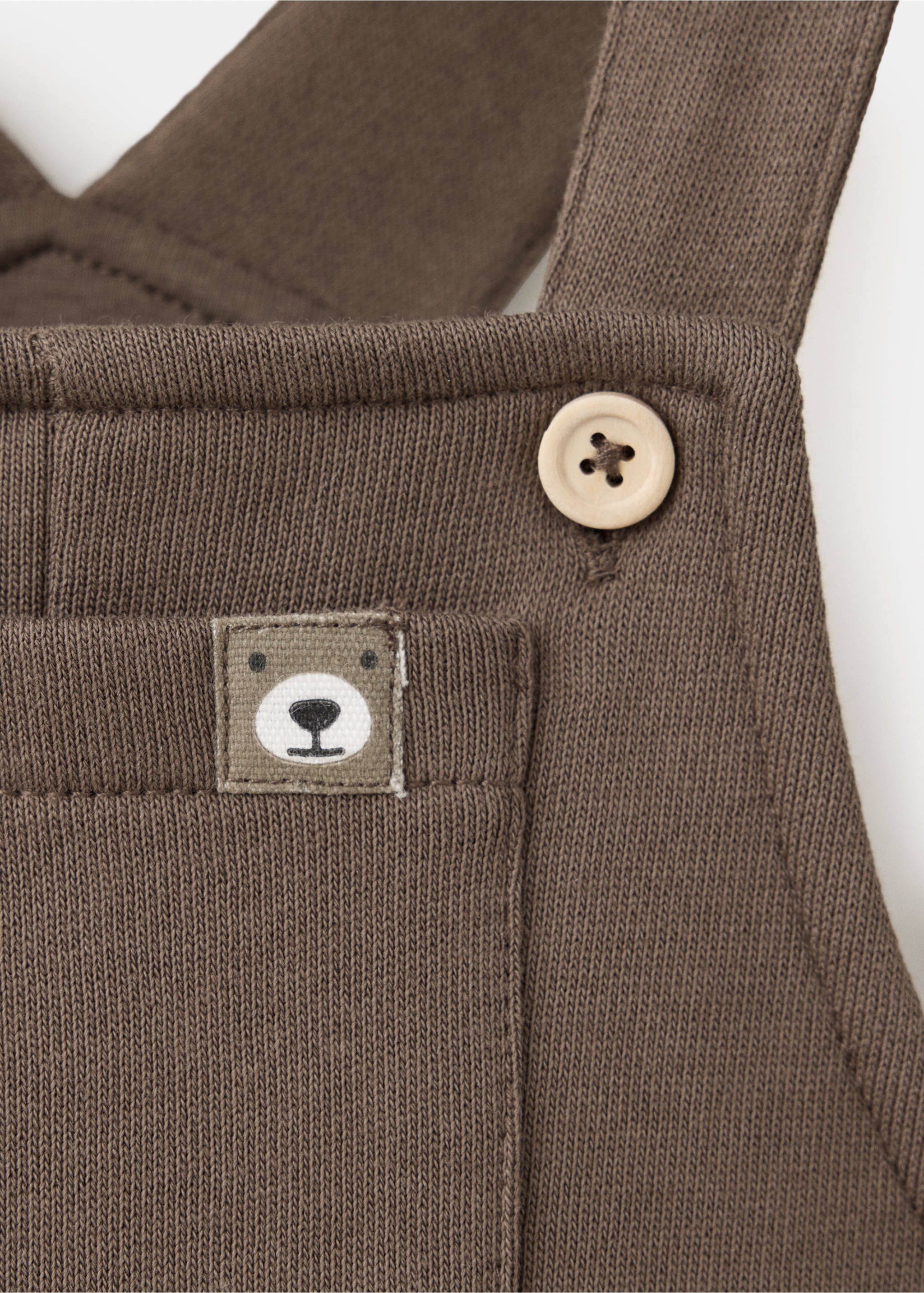 Brown knit children's dungarees close-up showing pocket and bear label., Chocolate. Ref: 37067925-00.