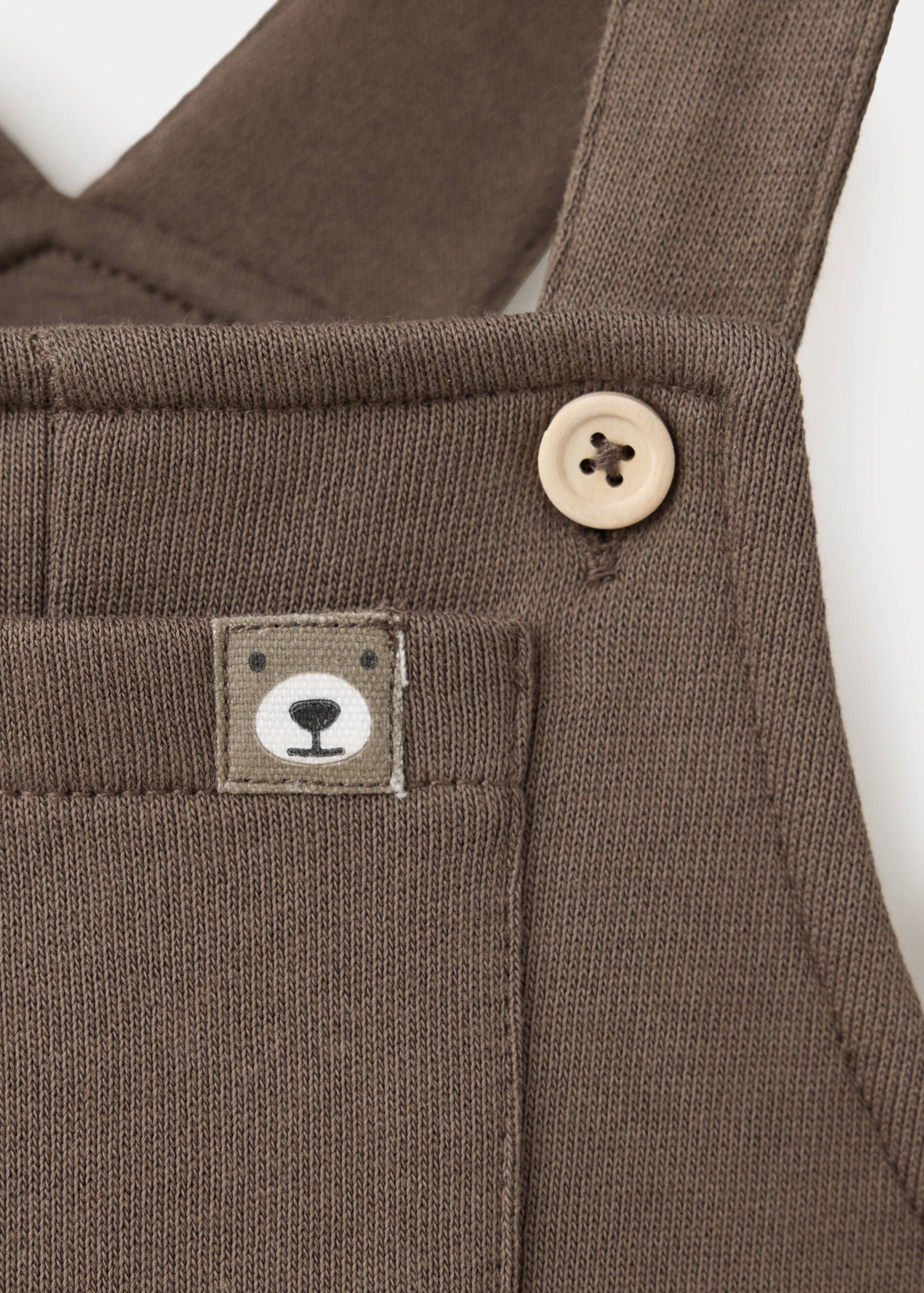 Brown knit children's dungarees close-up showing pocket and bear label.