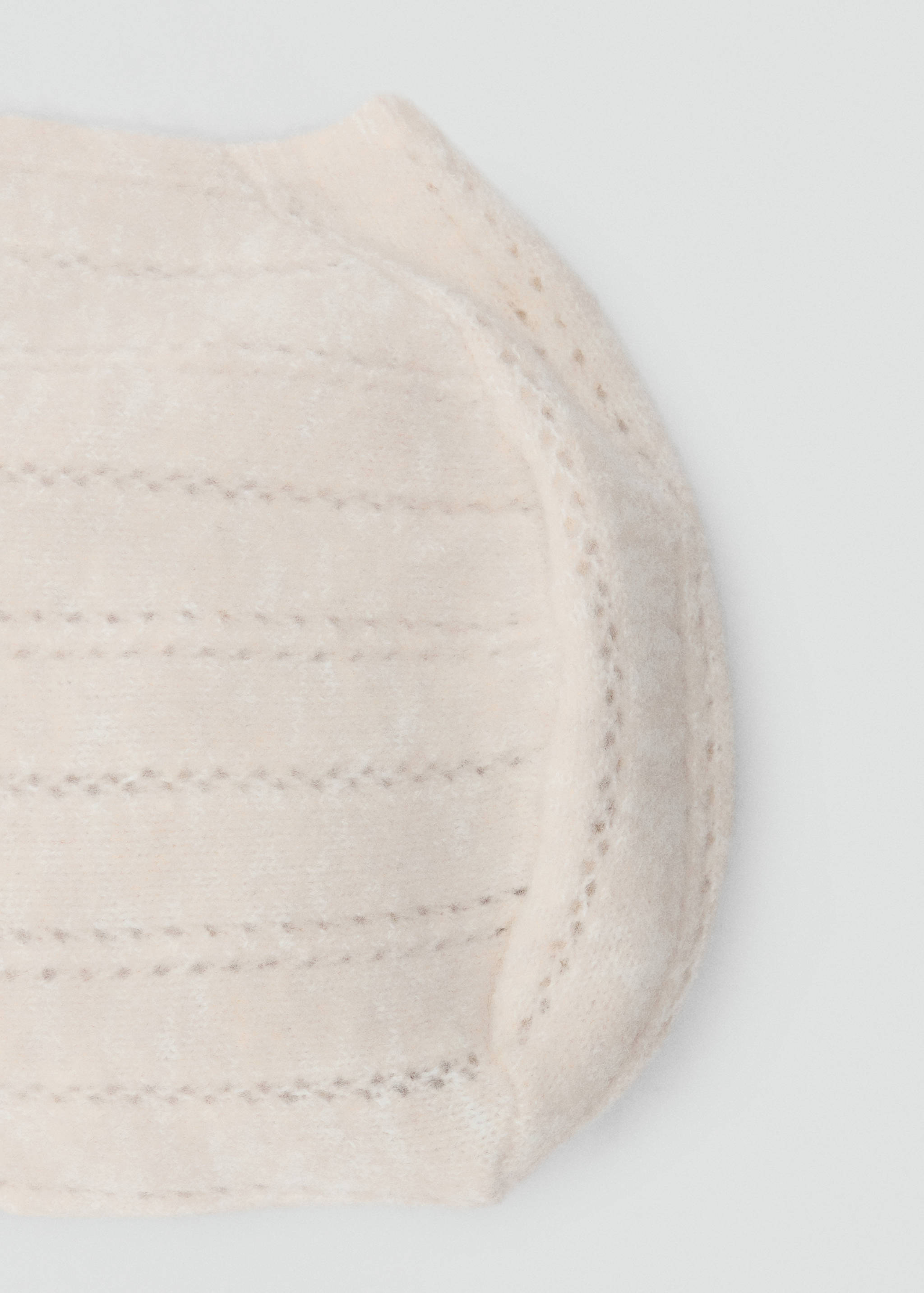 Close-up detail of a beige knit hat with ribbed texture and eyelet trim.