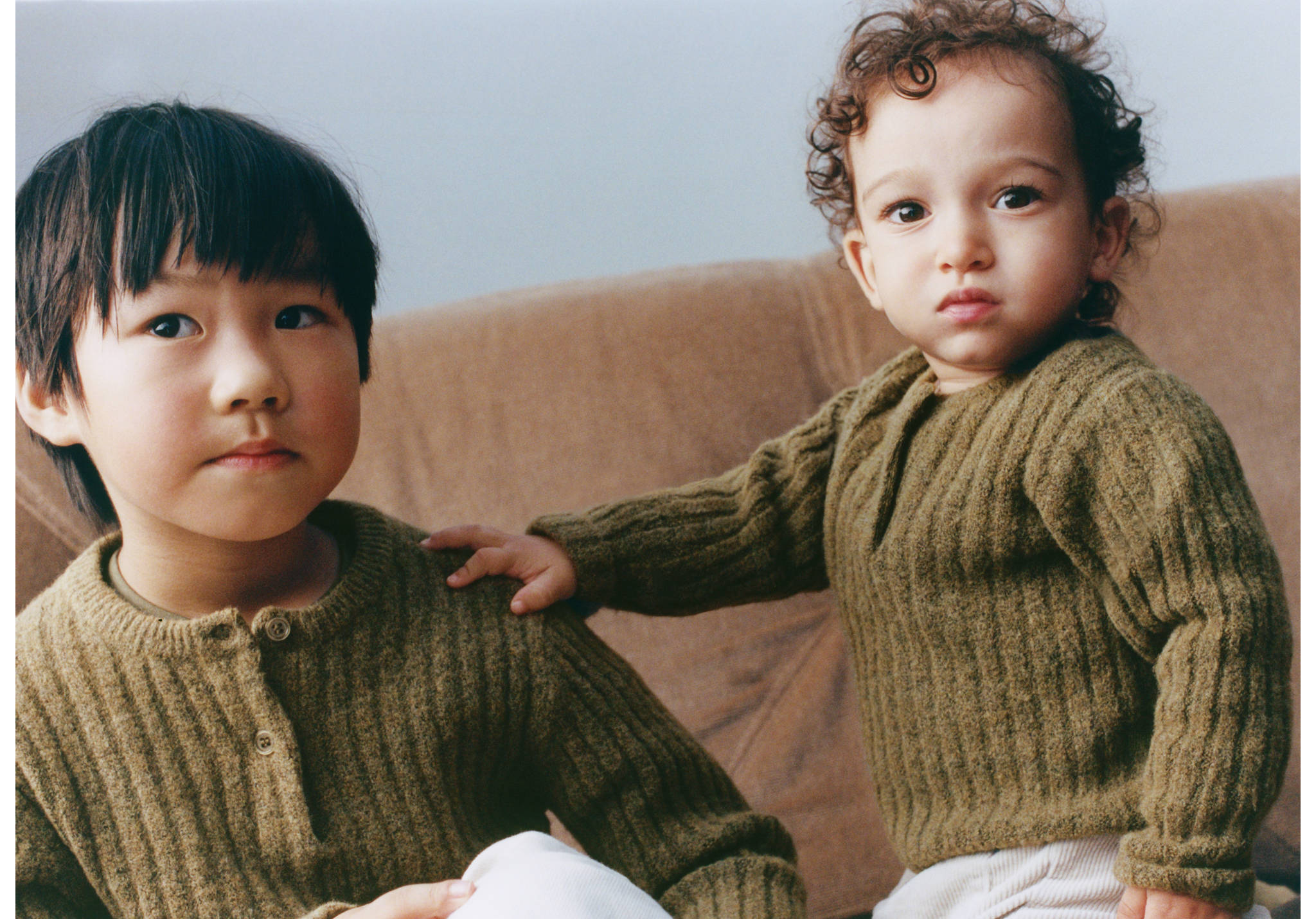 Two children wearing matching olive green ribbed knitted jerseys.