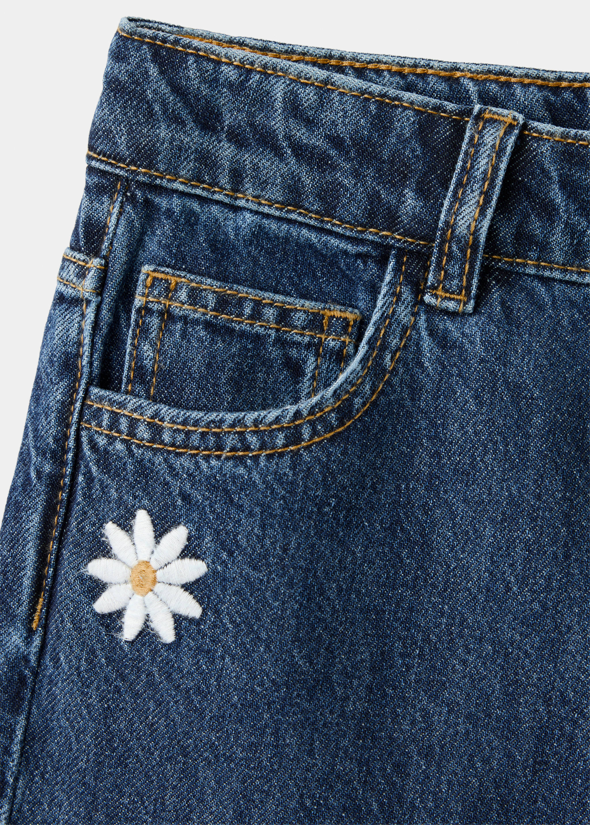 Close-up of dark blue denim trousers with a daisy embroidery.