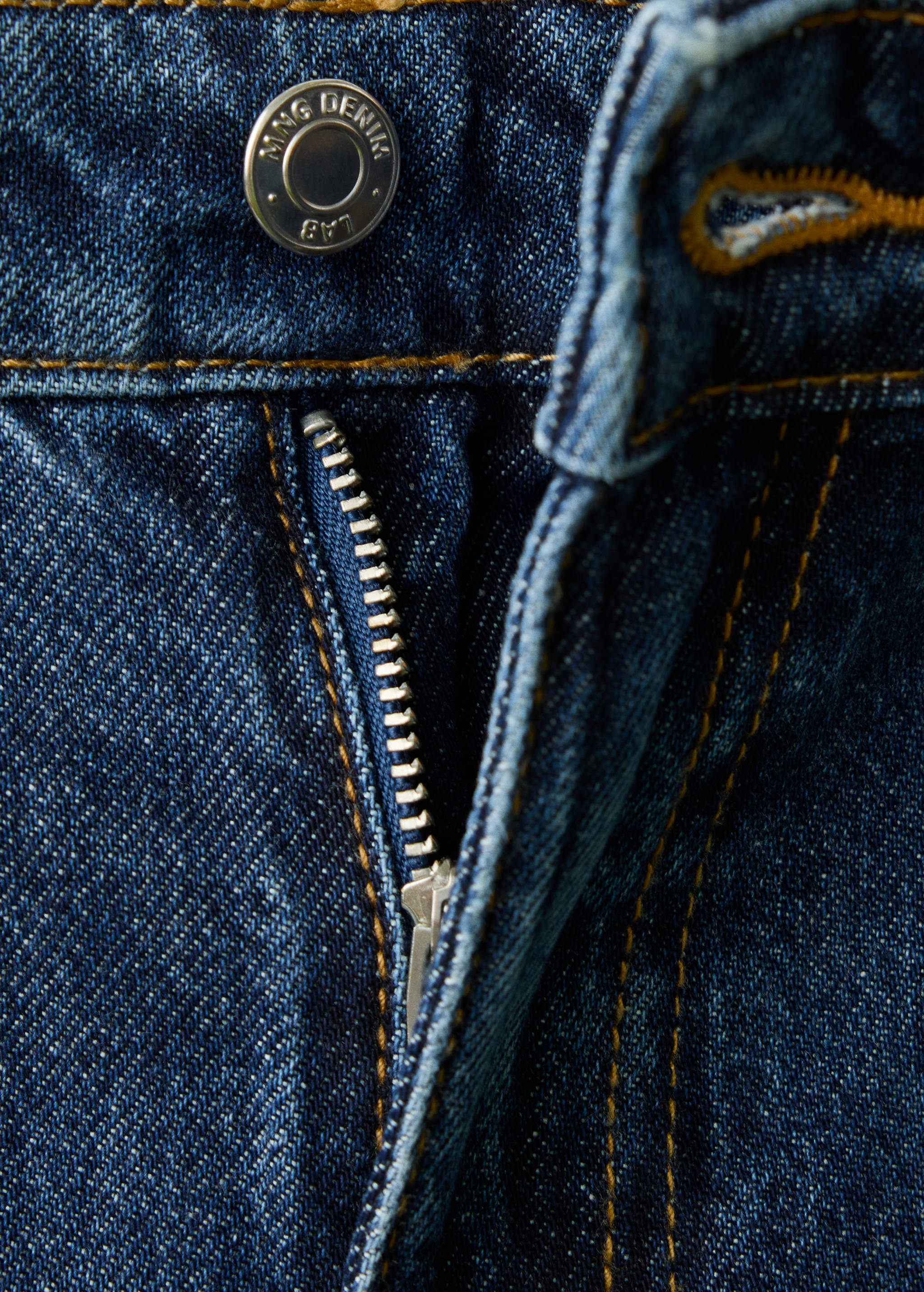 Close-up of dark blue denim trousers featuring a button and zip fly detail.