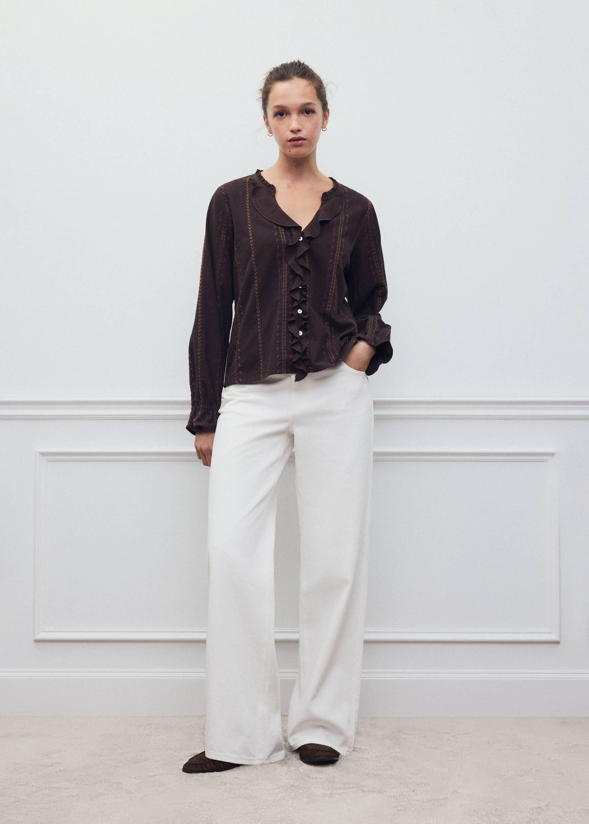 Brown shirt with ruffles and embroidery, worn with white trousers.