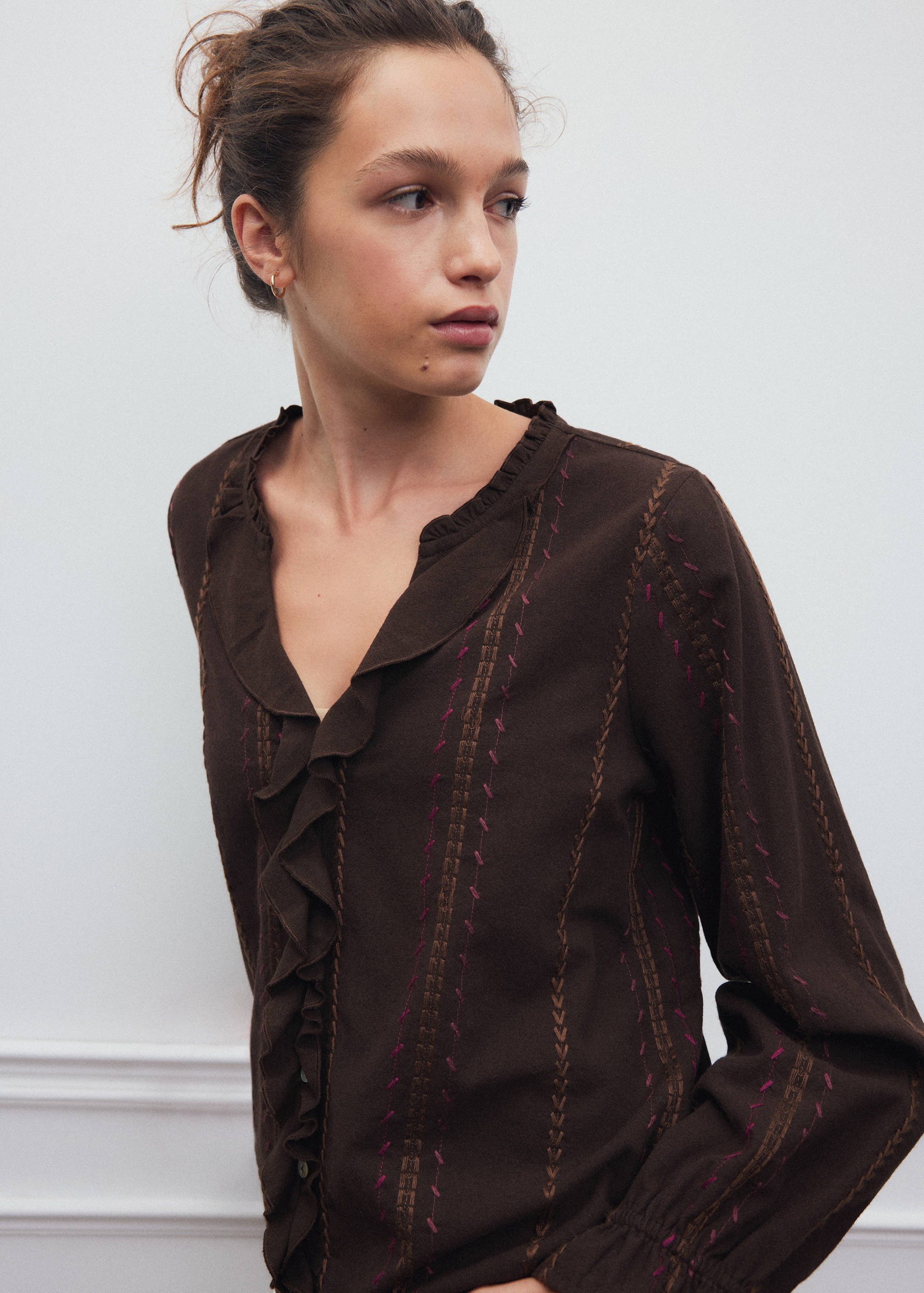 Brown long-sleeved shirt with embroidery and ruffled trim.