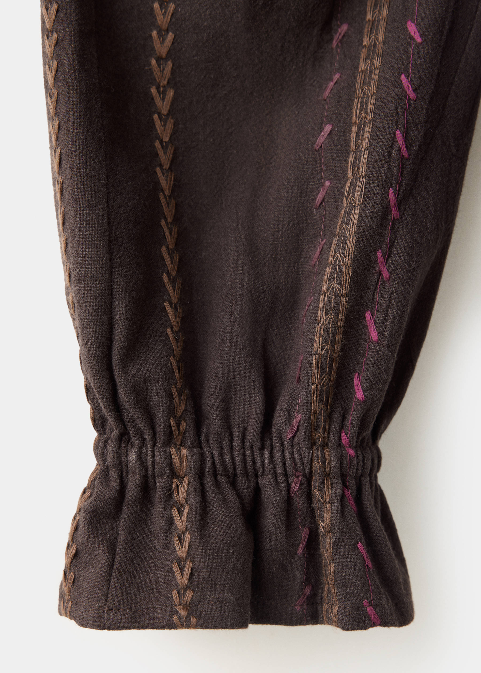 Dark brown shirt sleeve fabric showing textured vertical embroidery and a ruffled elastic cuff.