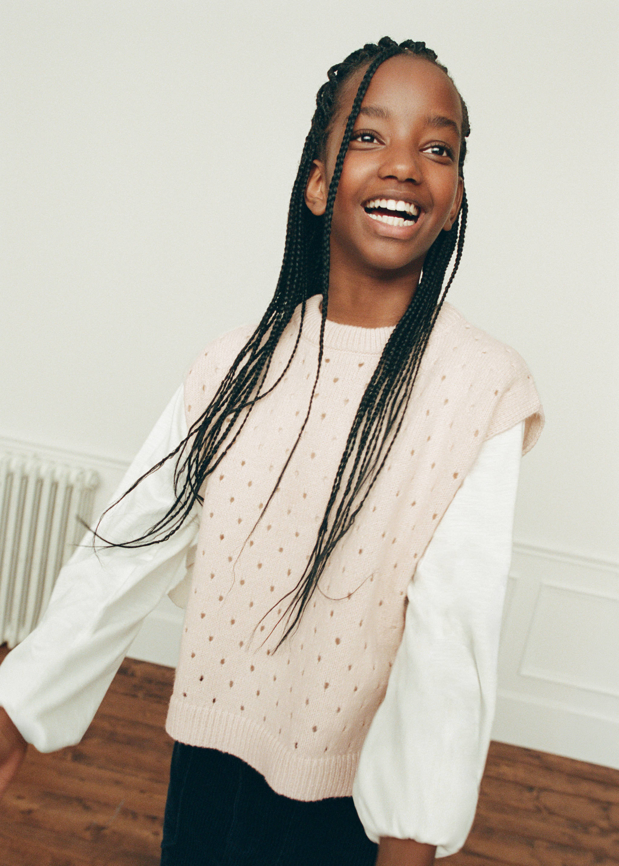 Pale pink knit sweater vest with pointelle pattern, layered over a white top.