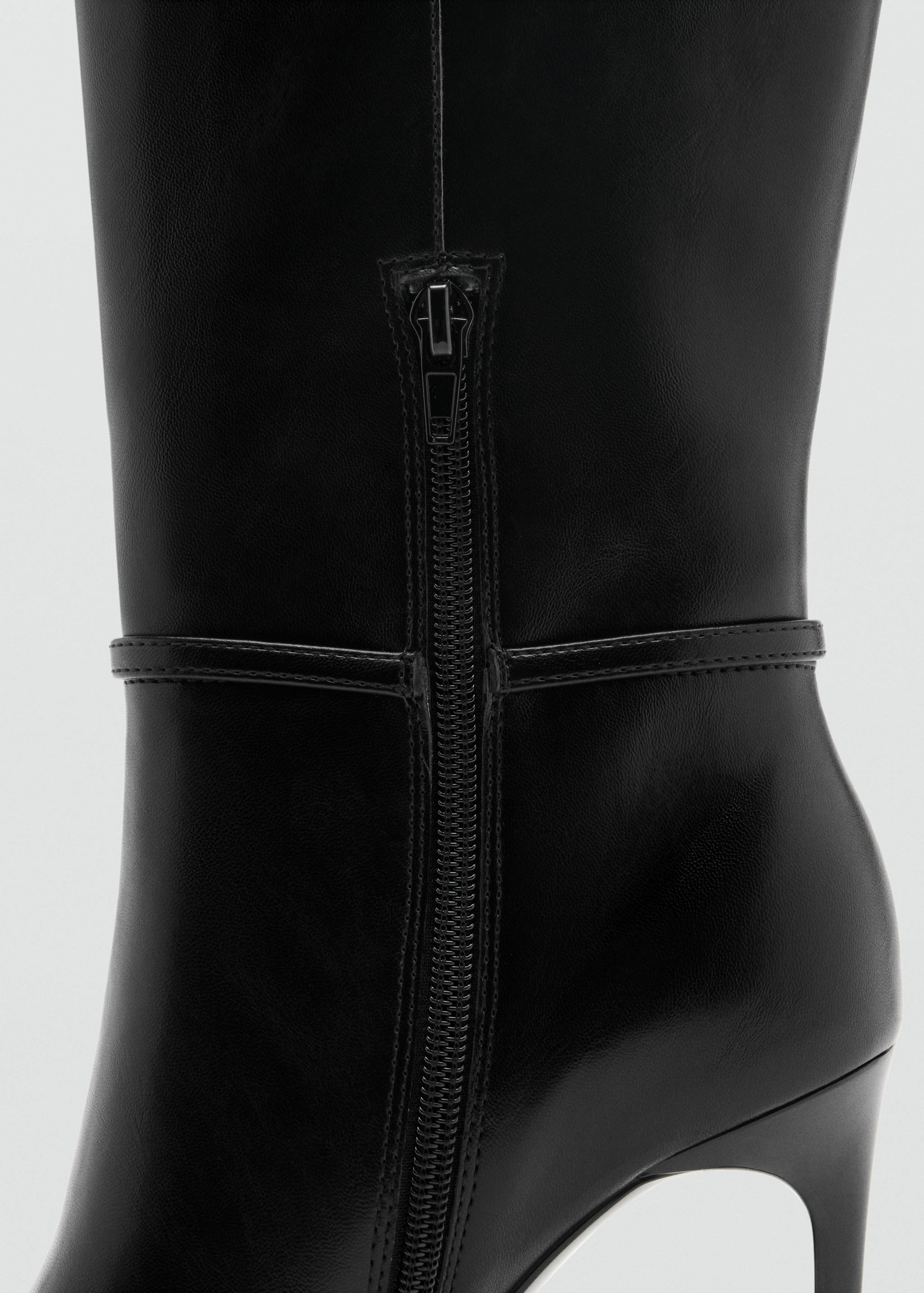Close-up of a black high-heeled boot showing the side zipper and ankle strap.