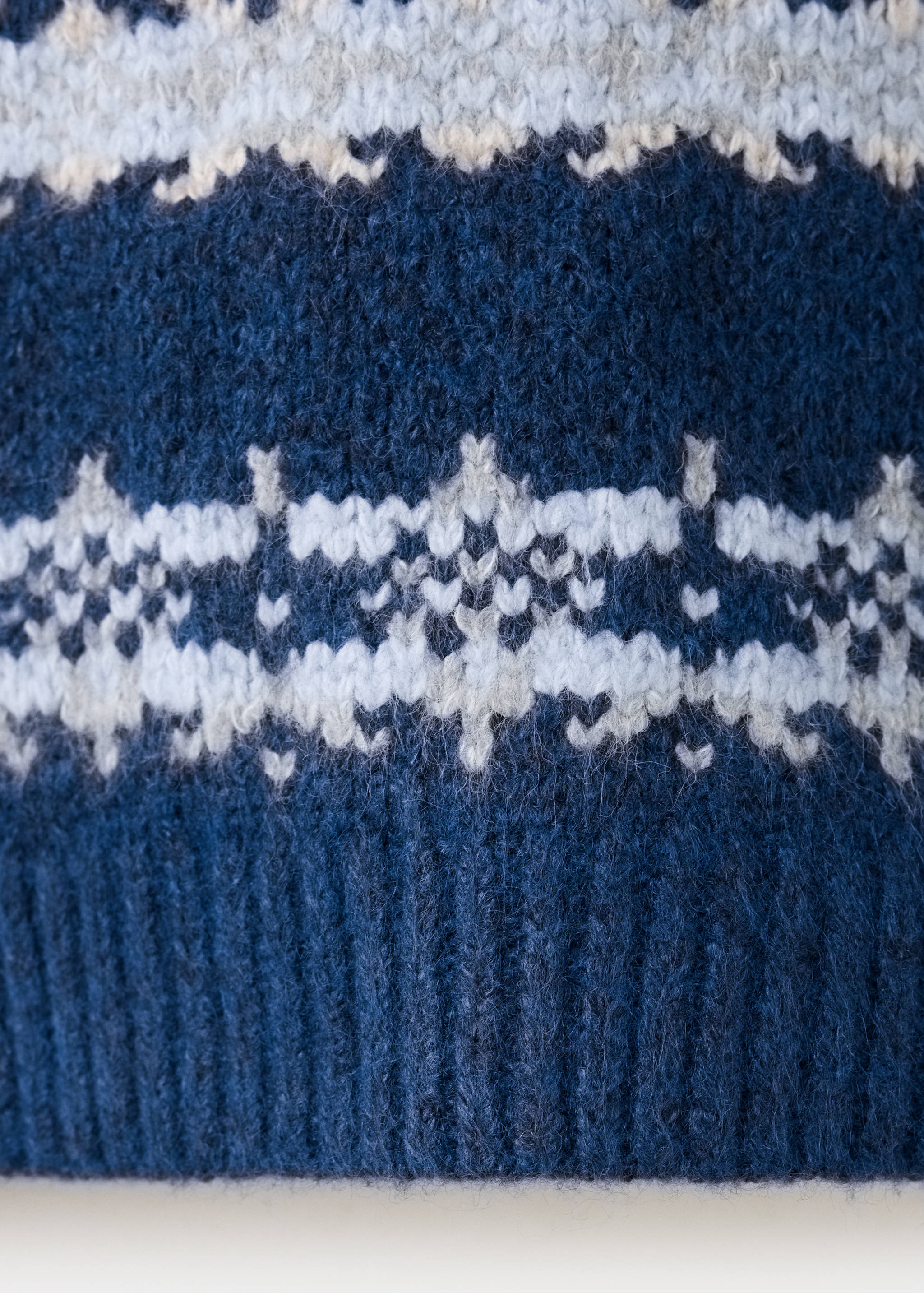 Close-up of a blue knit jersey featuring a white and grey Fair Isle pattern.