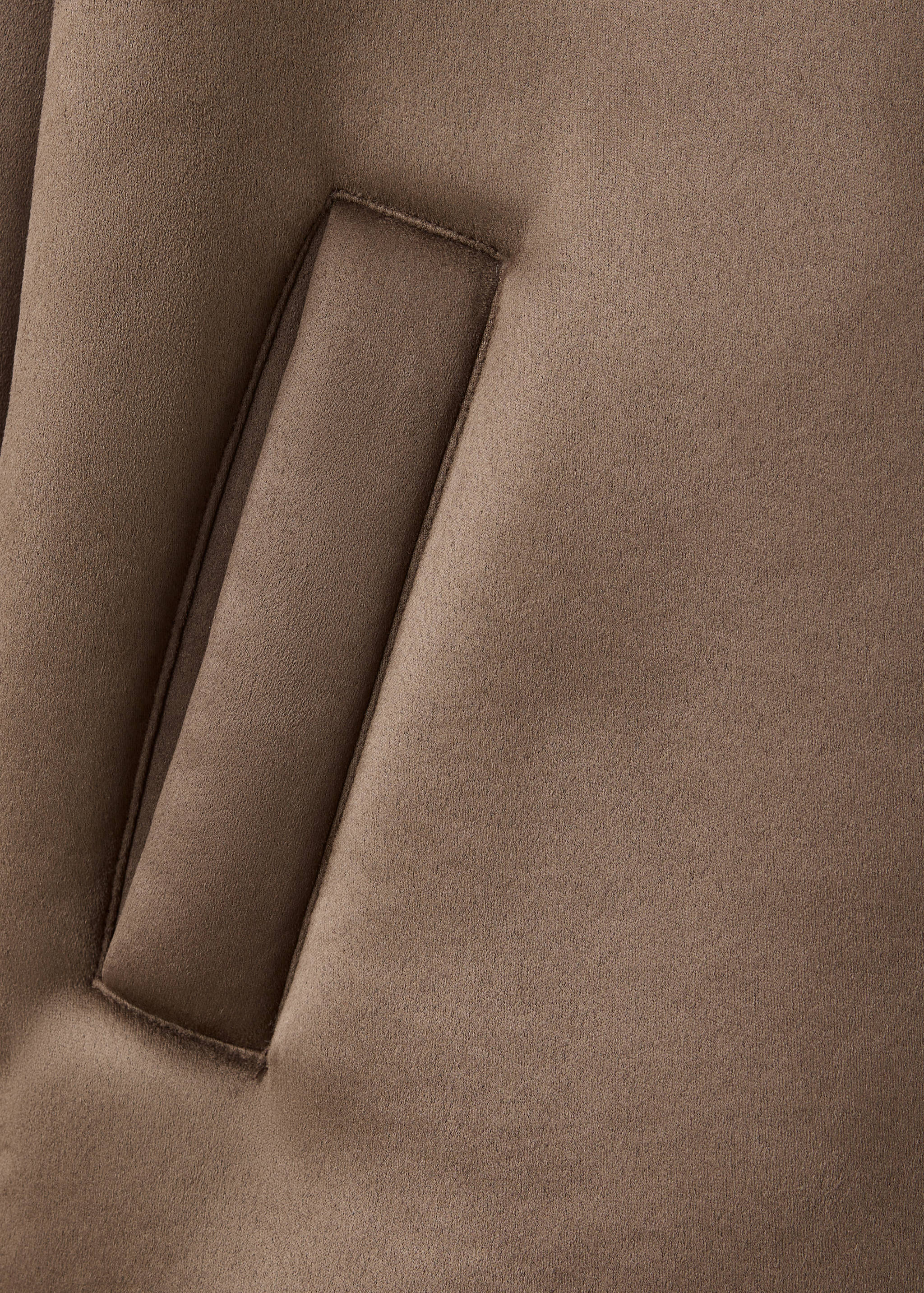 Close-up of the fabric and welt pocket detail on a brown coat.