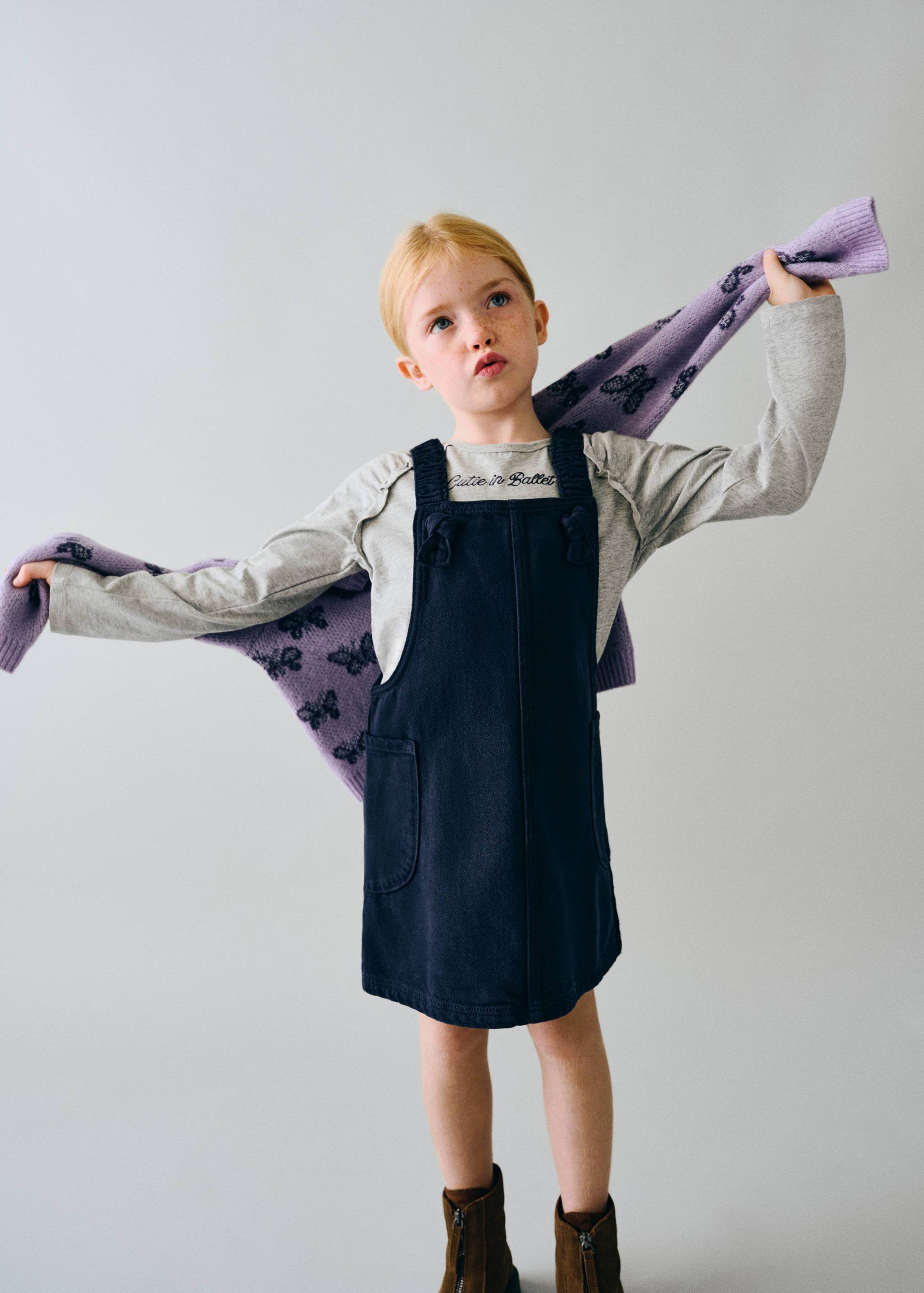 Dark blue pinafore dress layered with a grey long-sleeved t-shirt and purple scarf.