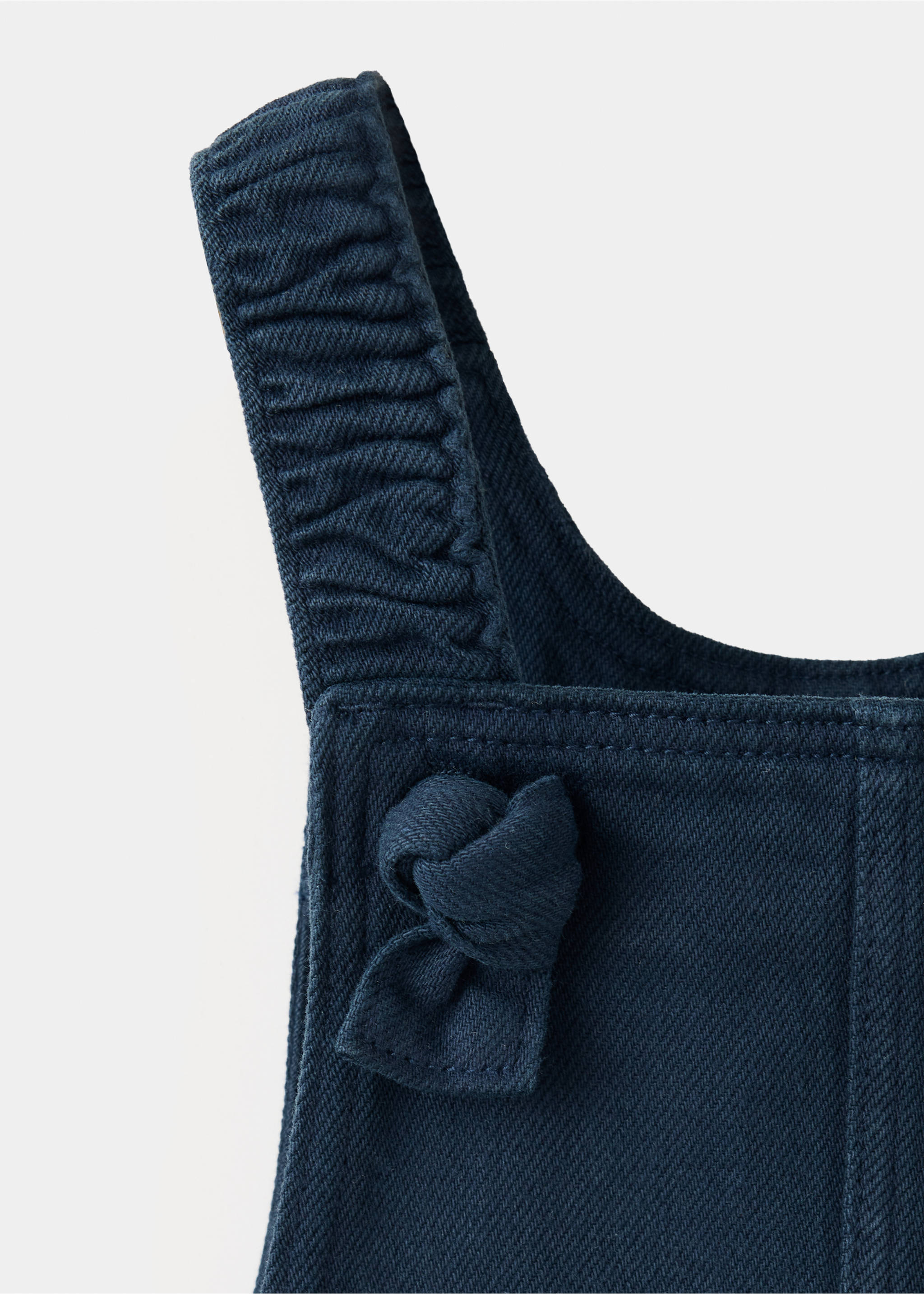 Close-up of a dark blue denim kids pinafore with a knotted strap., Navy. Ref: 37068284-00.