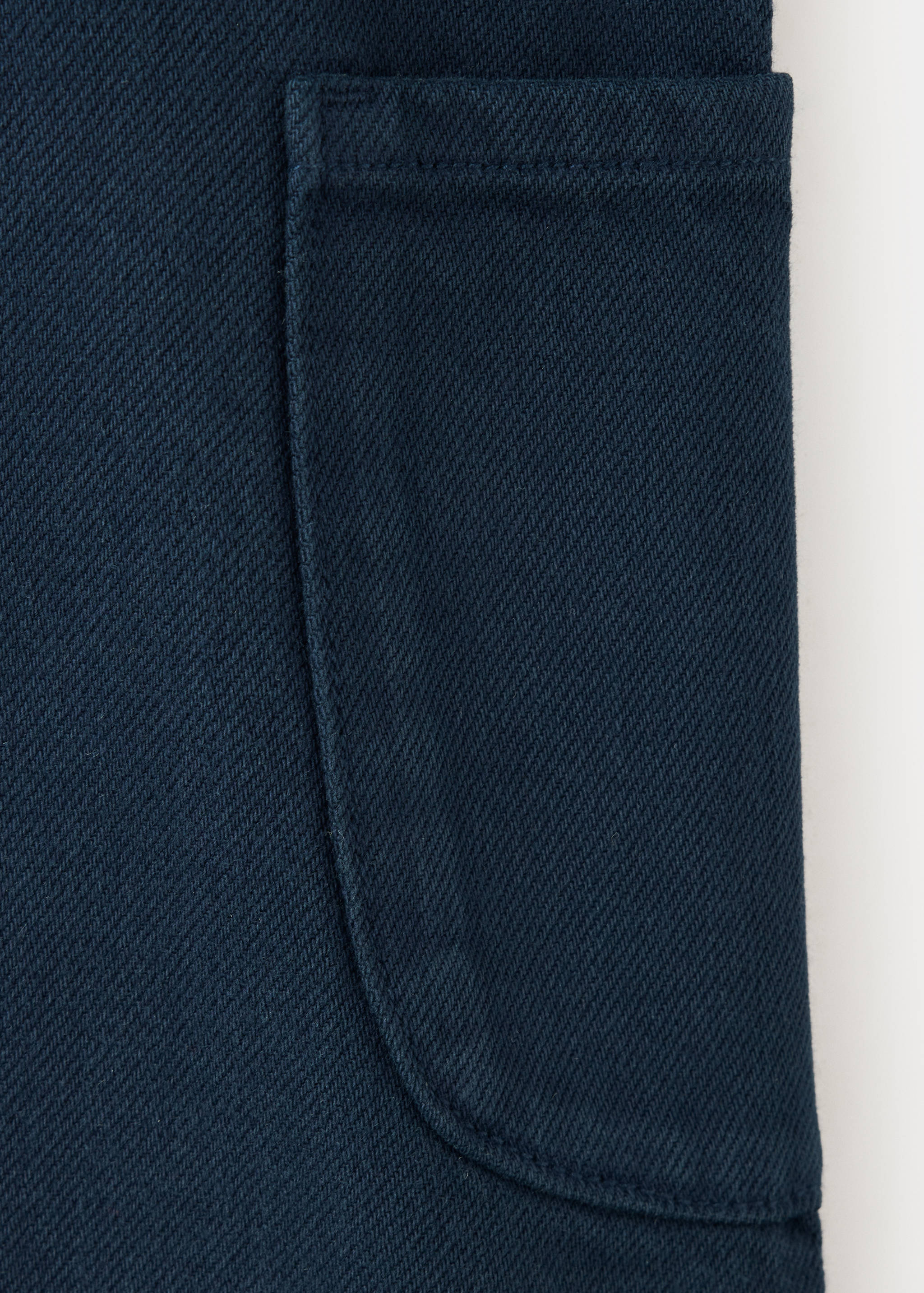 Navy blue denim fabric detail of a kids pinafore with a patch pocket.
