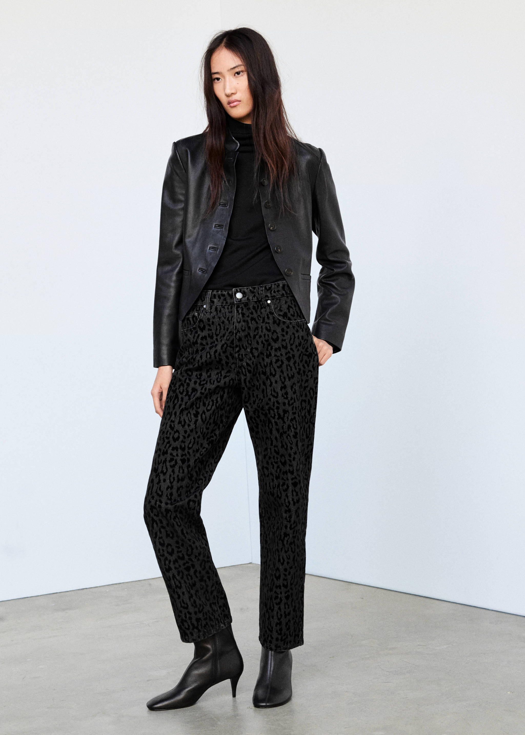 Black animal print denim trousers with a straight fit and ankle length, styled with a black jacket and top.