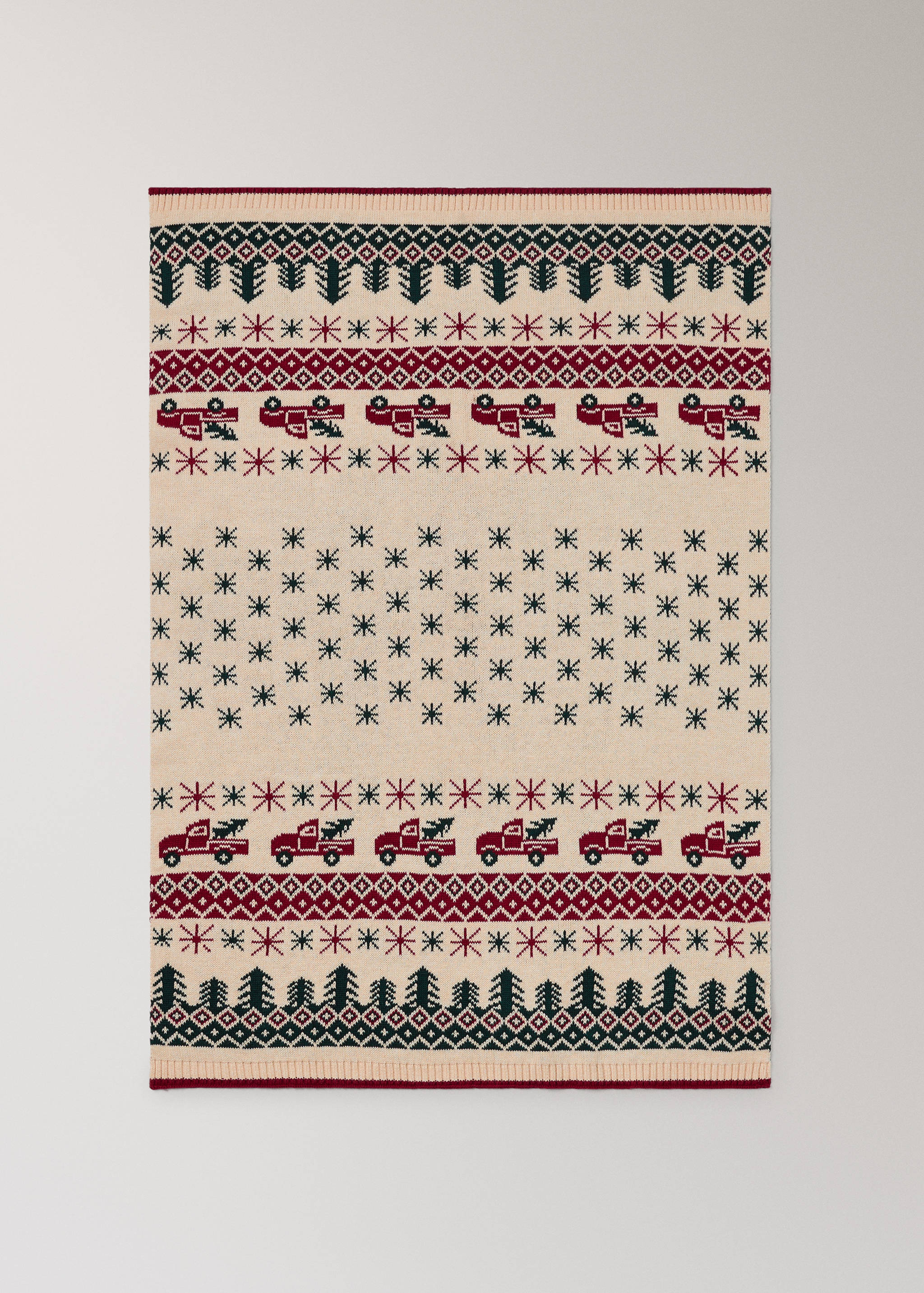 Cream knitted blanket with a festive red and green tree and truck pattern.