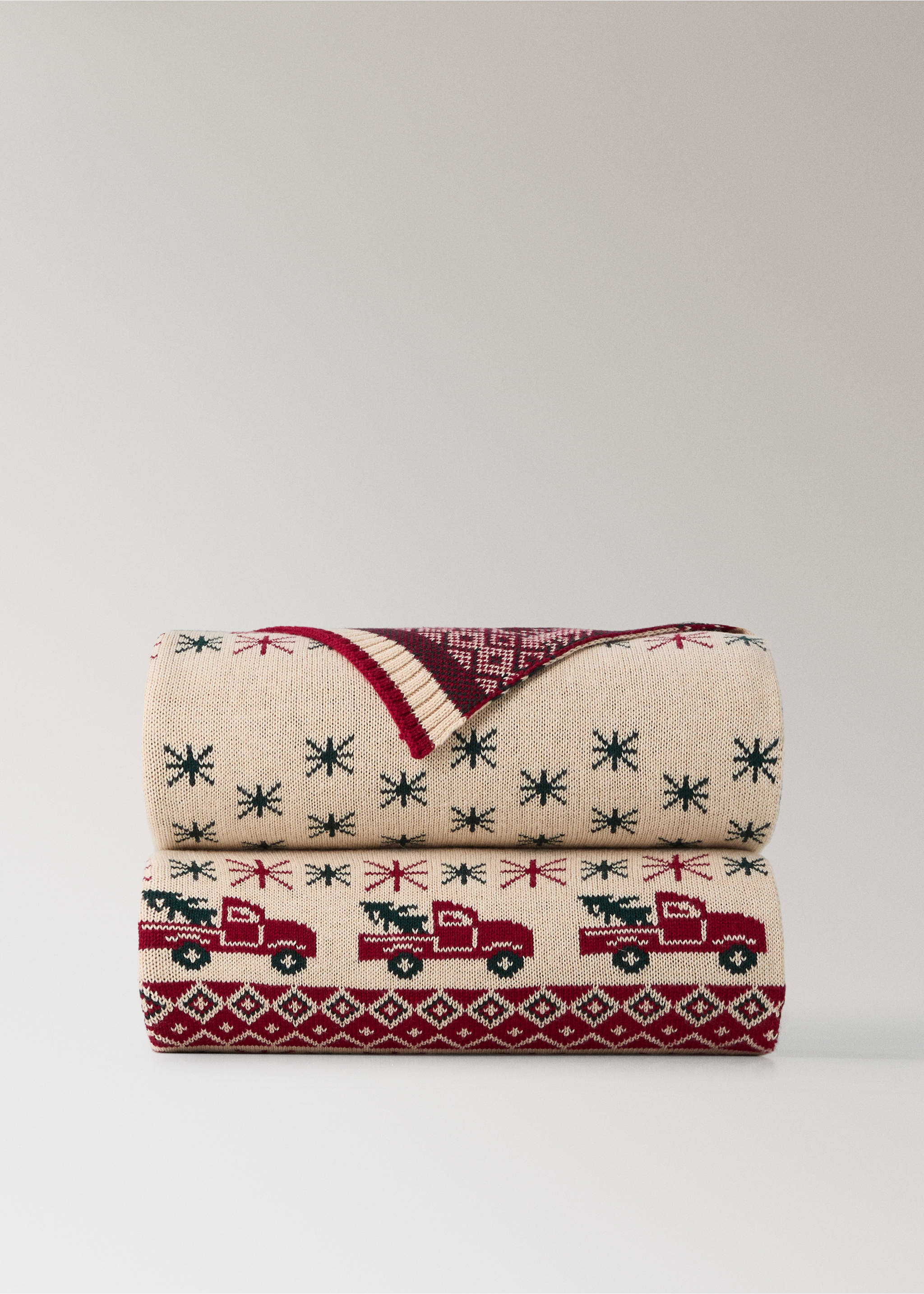 Folded cream knit blanket with a festive red and green truck and snowflake pattern., Red. Ref: 37068630-00.