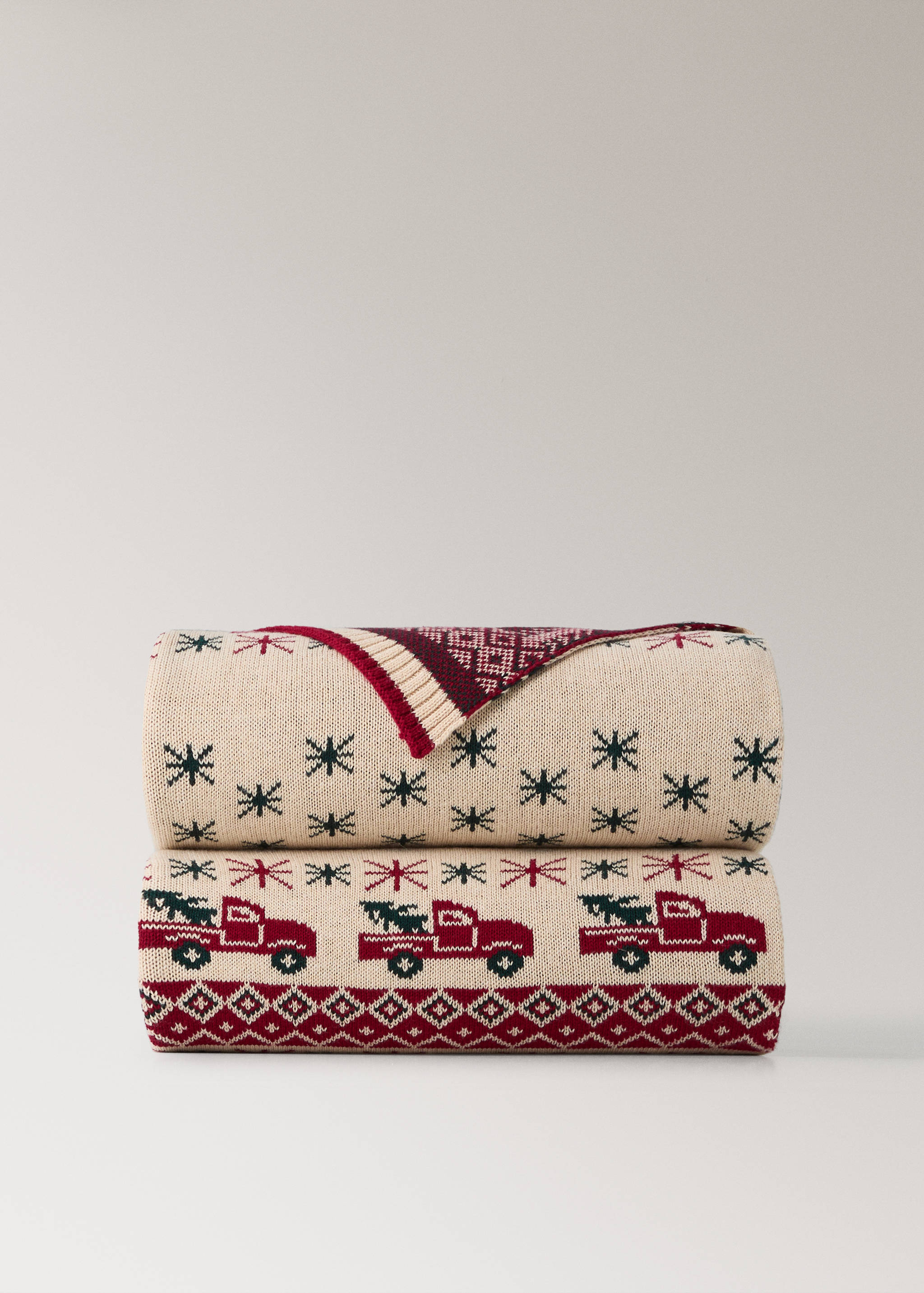Folded cream knit blanket with a festive red and green truck and snowflake pattern.