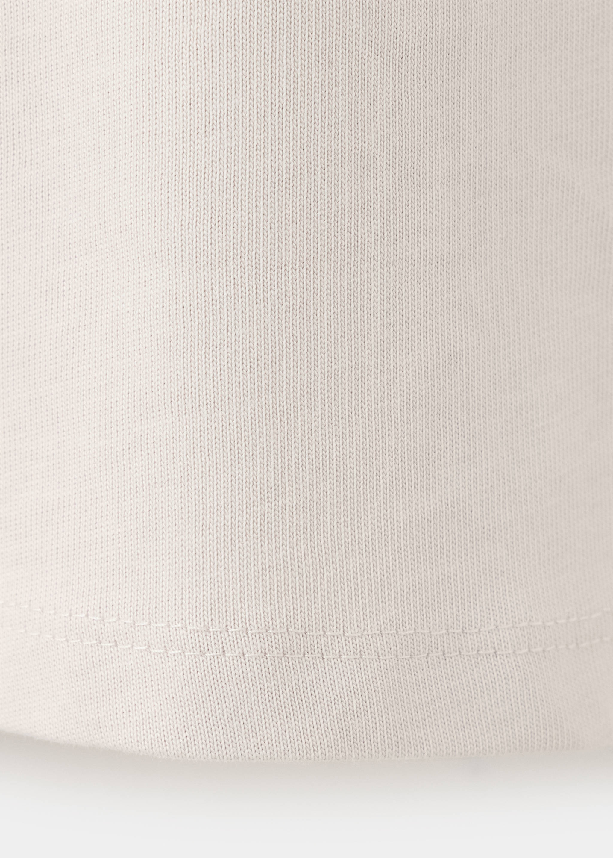 Close-up of the fine-knit fabric and hem of a light beige kids' polo.