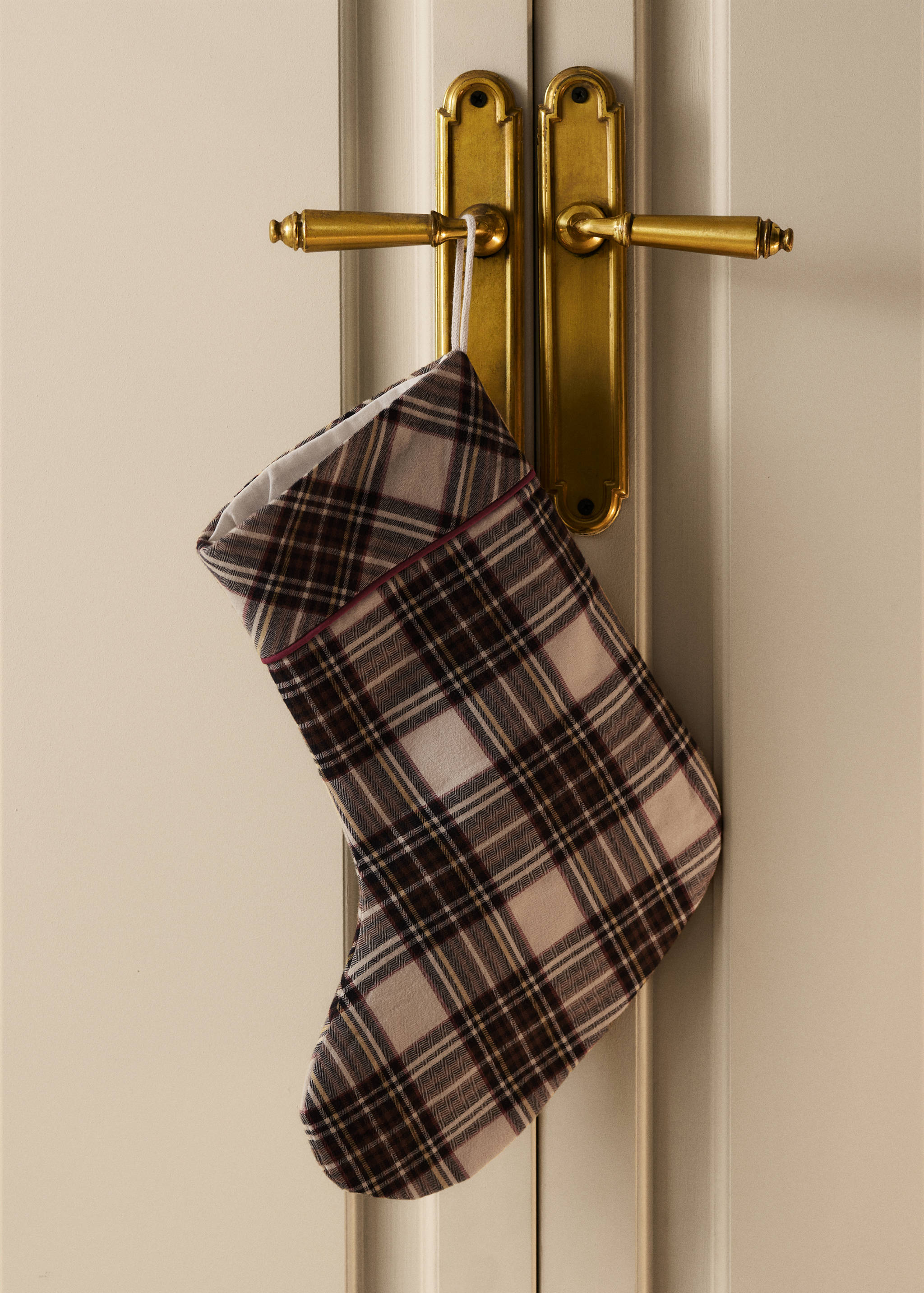 Plaid Christmas stocking in beige, brown, and dark red hanging from a brass door handle.