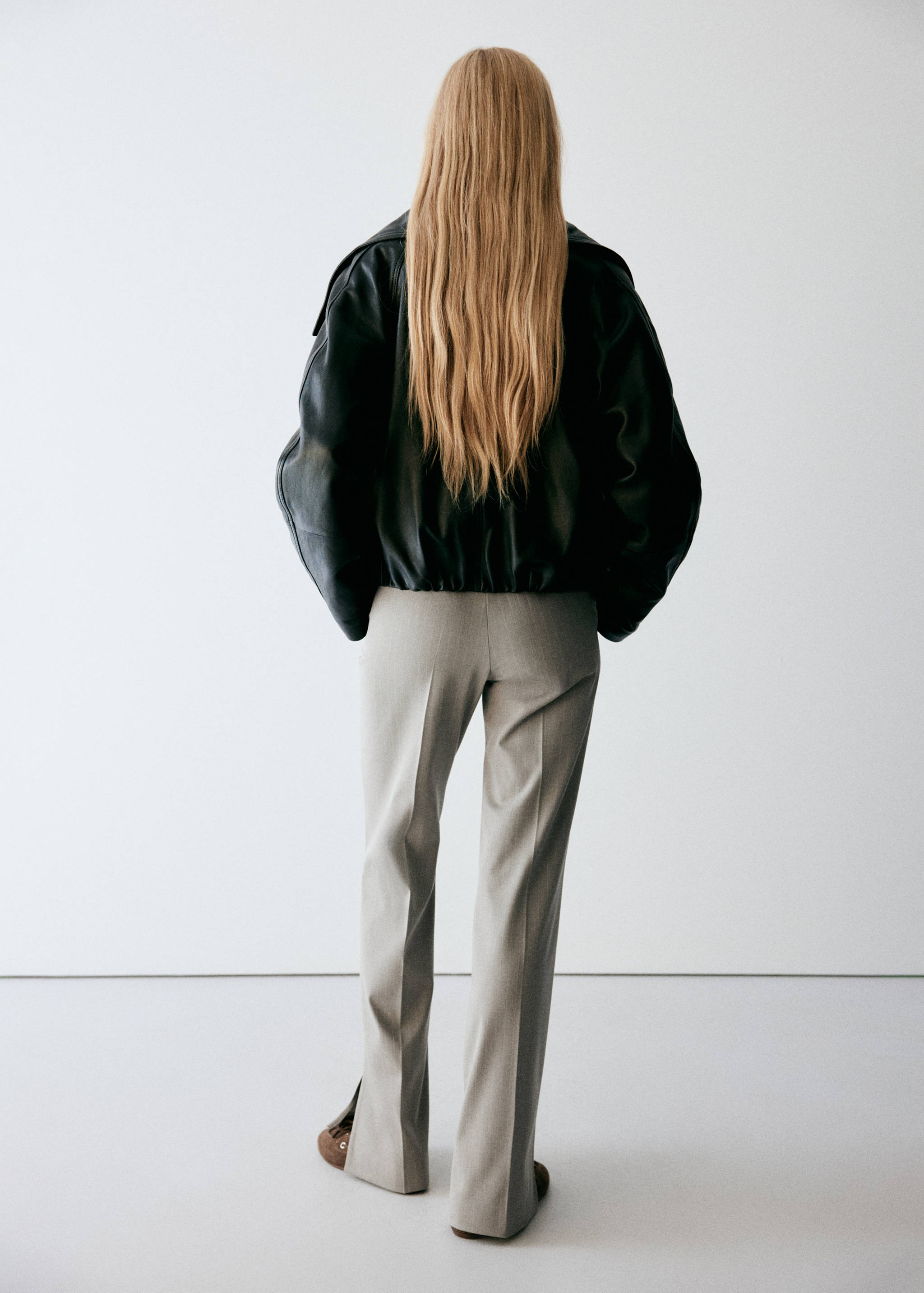 Grey trousers with pressed creases and hem slits, seen from the back.