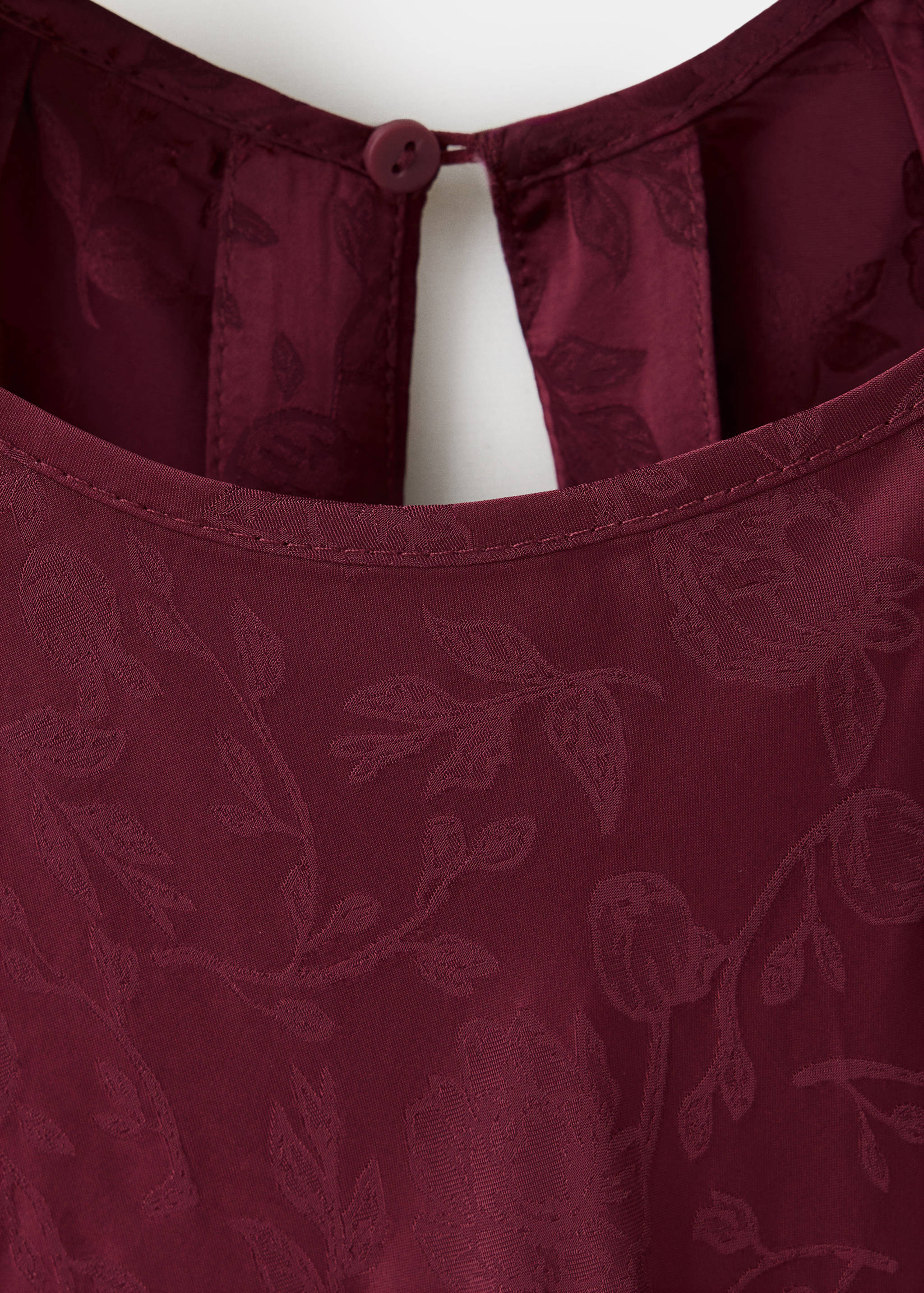Close-up of a maroon dress with a floral jacquard pattern and a buttoned keyhole back.