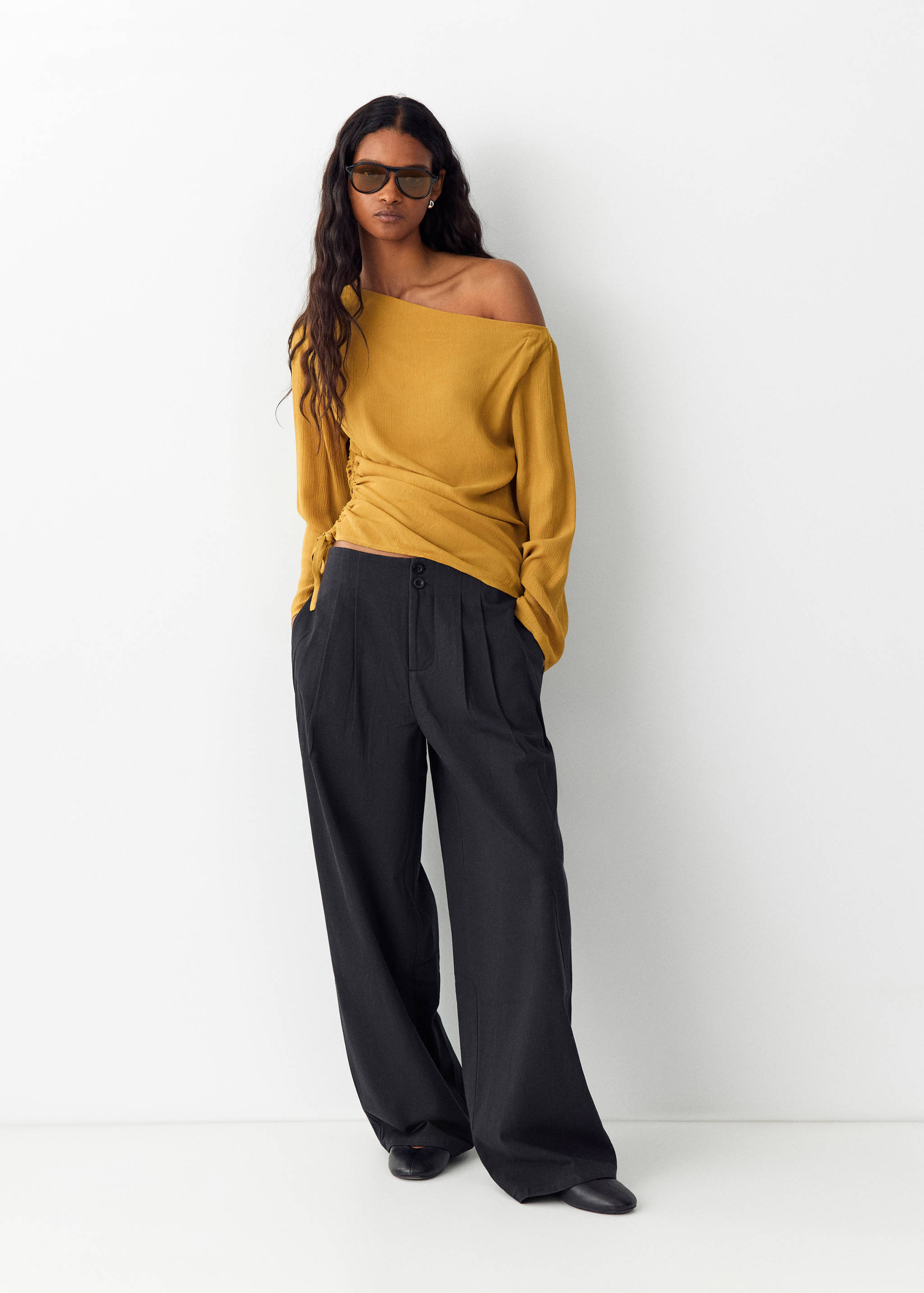 Dark grey wide-leg trousers with front pleats, worn with a mustard-yellow off-the-shoulder top.