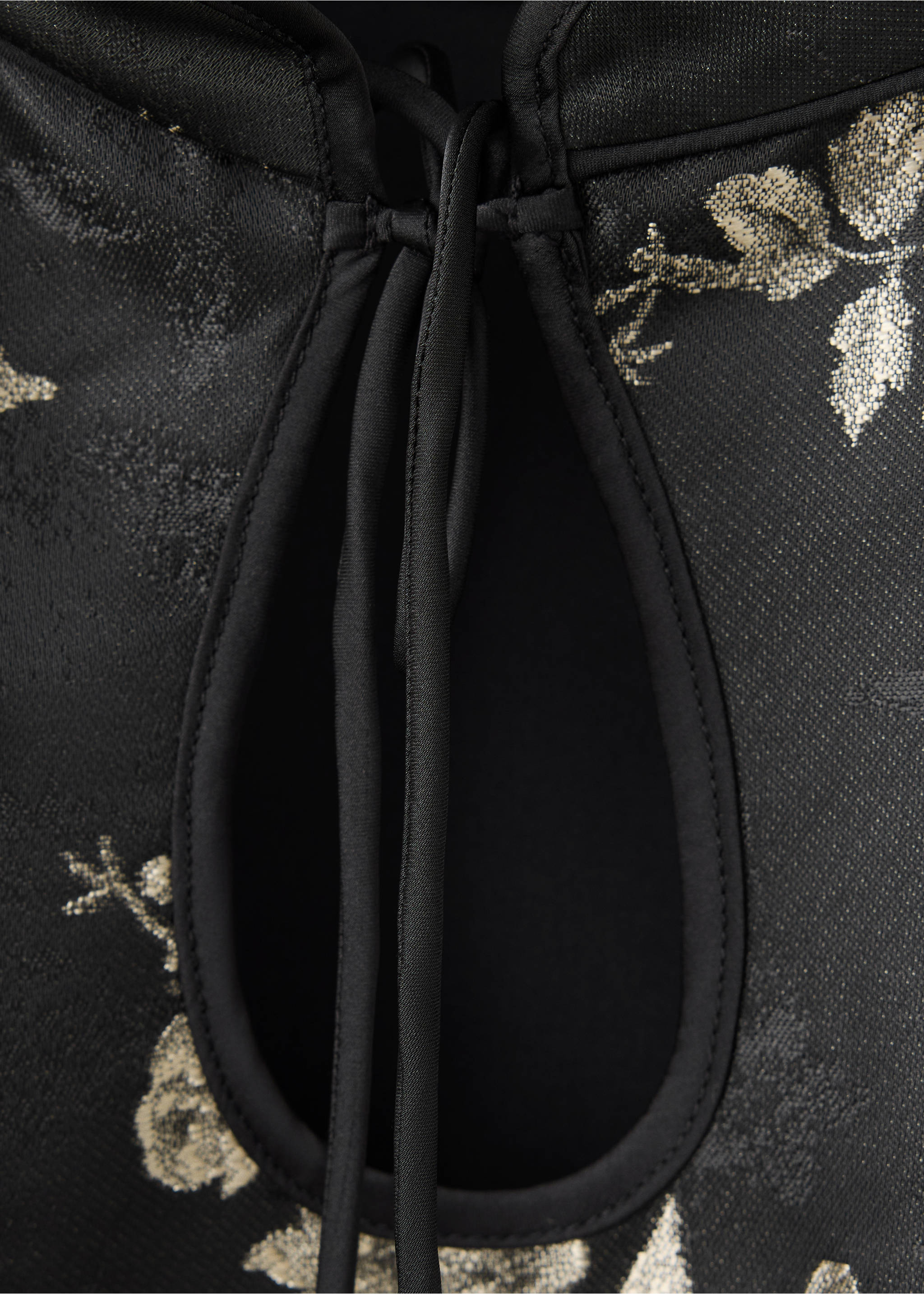 Close-up of a black dress with a keyhole neckline, tie closure, and metallic gold floral print., Black. Ref: 37069117-00.