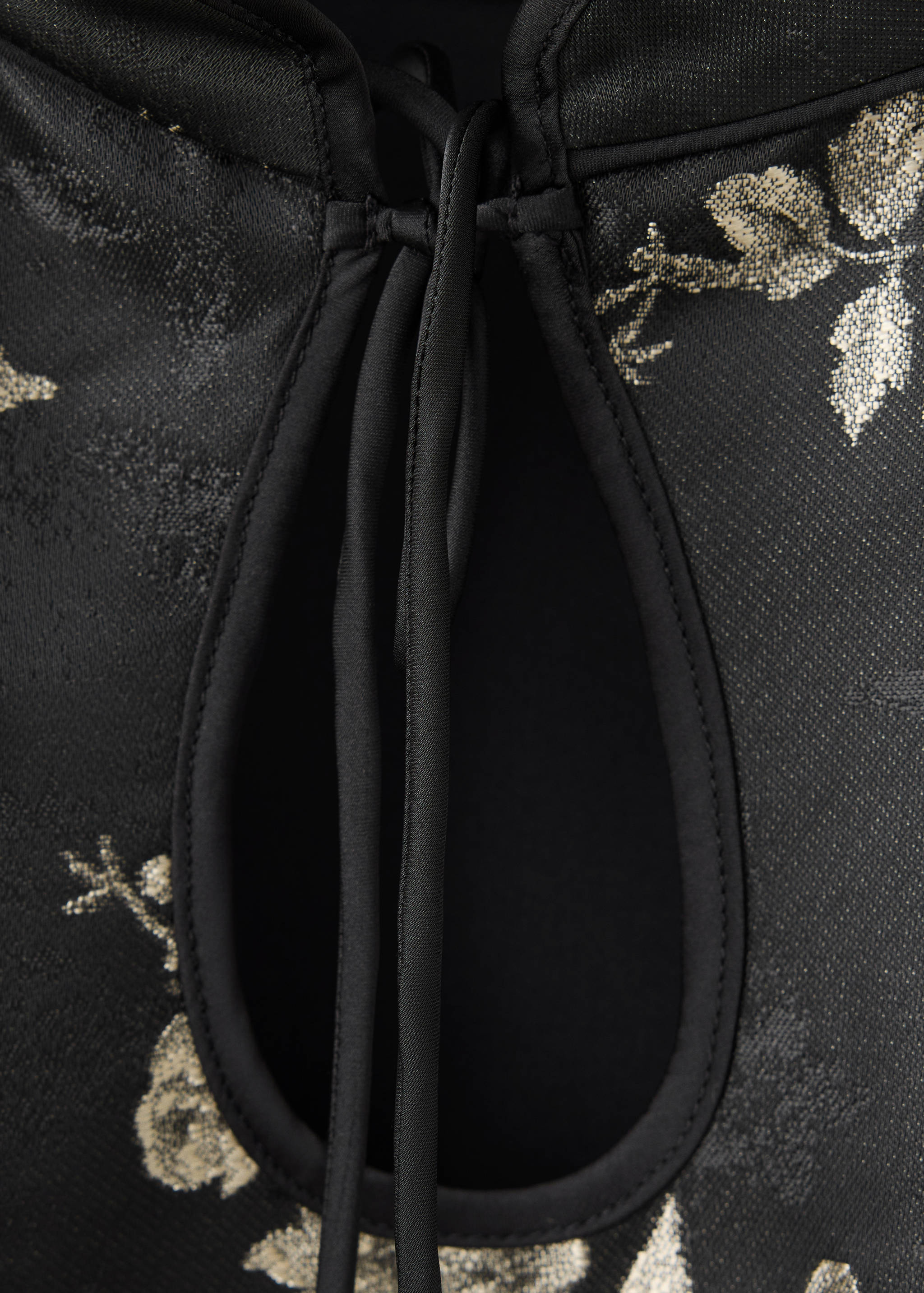 Close-up of a black dress with a keyhole neckline, tie closure, and metallic gold floral print.