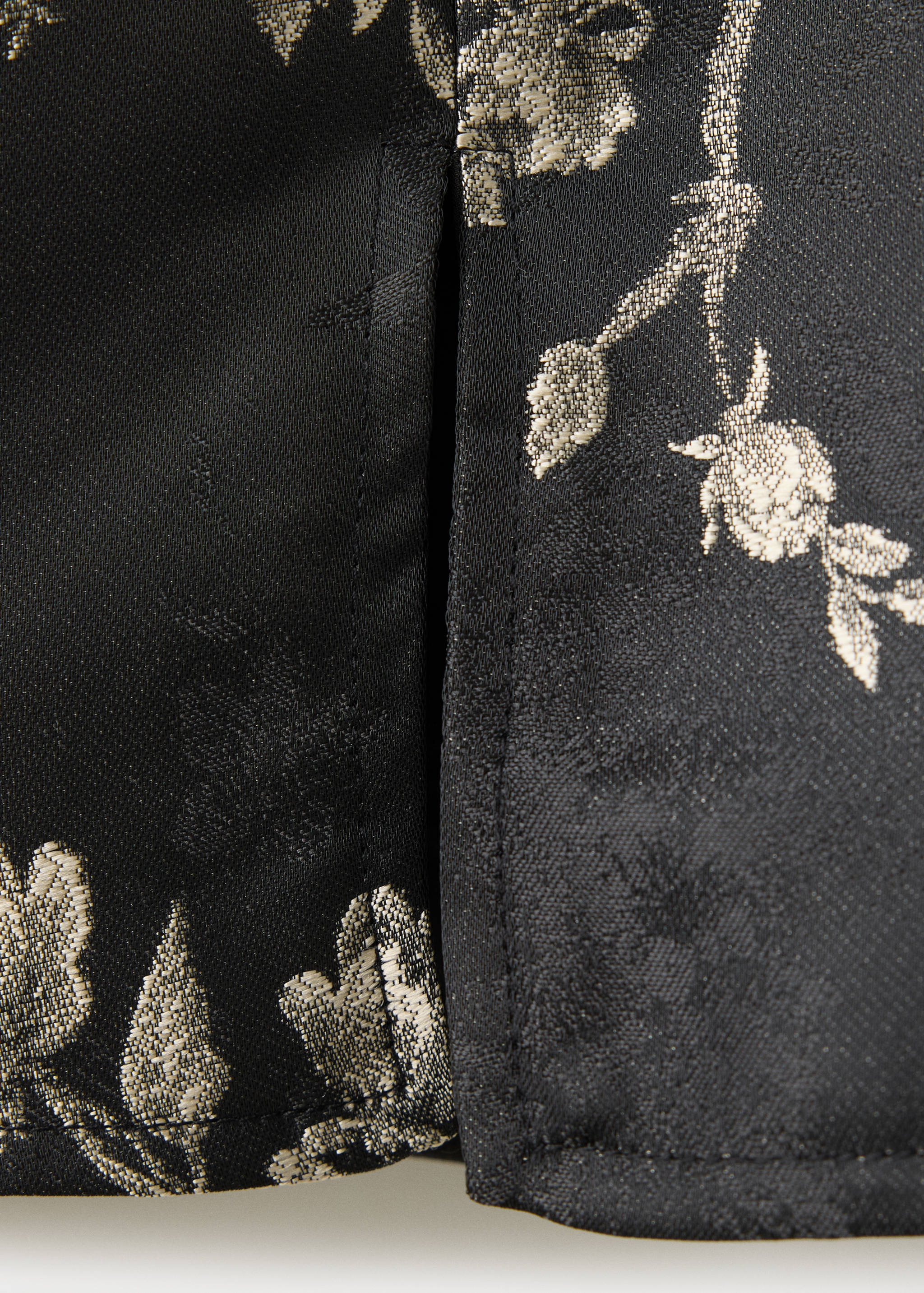 Close-up of black dress fabric with a metallic gold floral jacquard pattern.