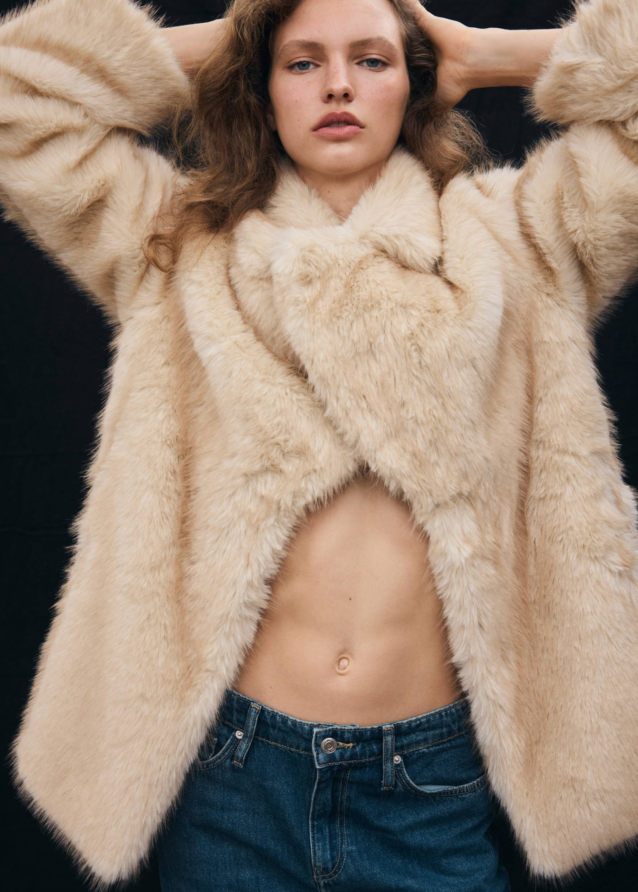 Beige faux-fur coat with wide lapels, worn open with blue jeans.
