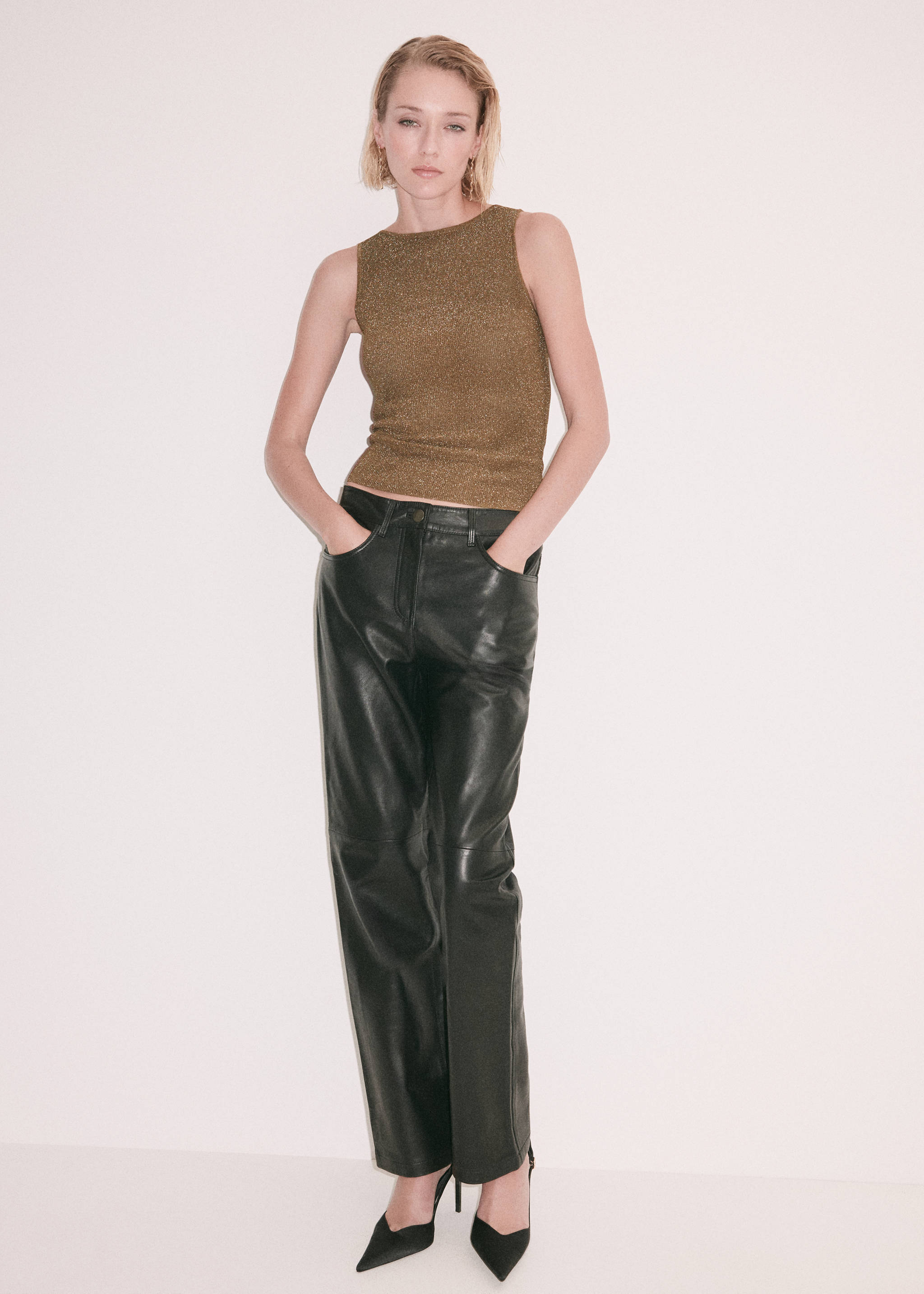 Metallic bronze-gold sleeveless fitted top with a boat neckline worn with black trousers.
