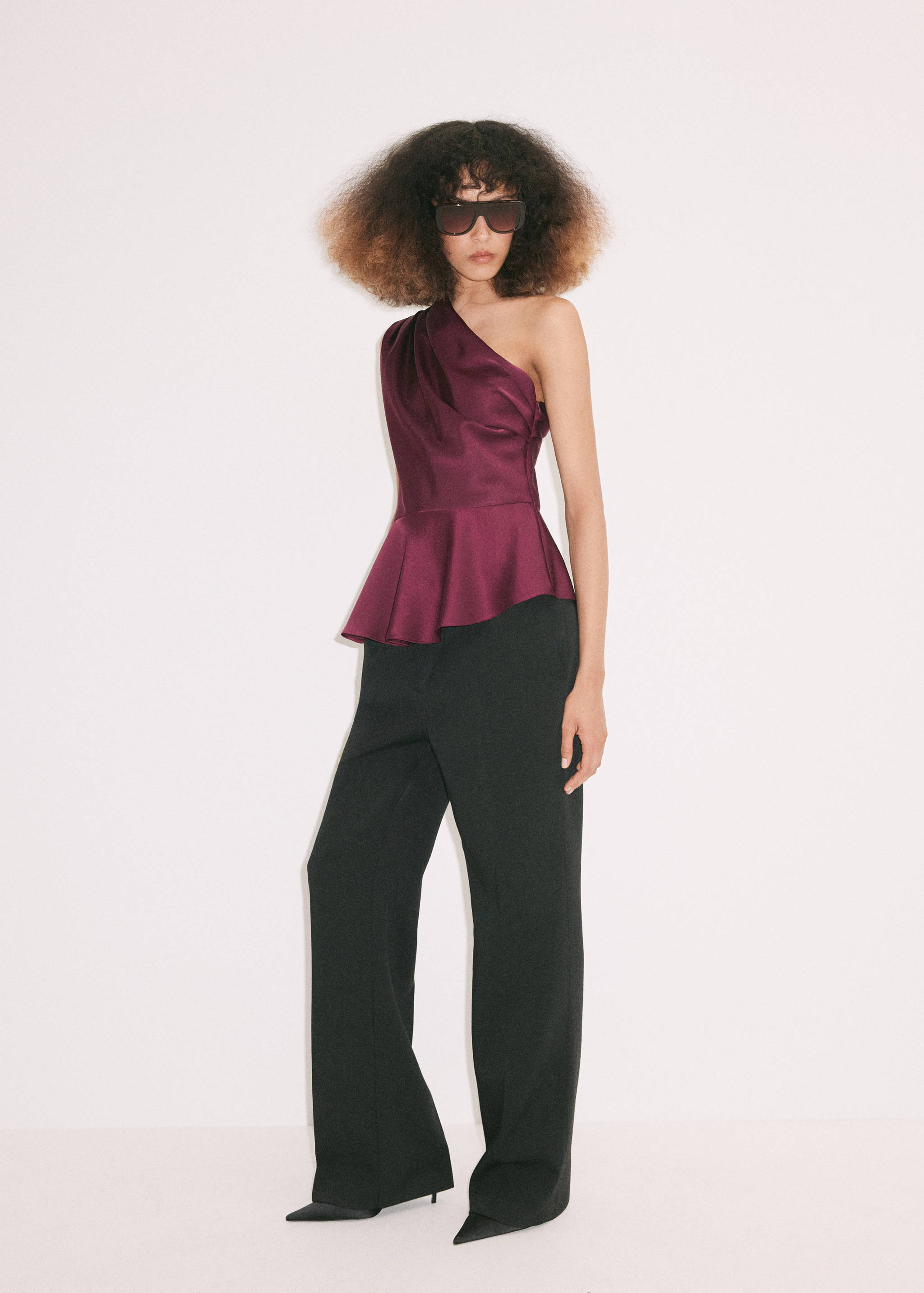 Plum-coloured one-shoulder satin blouse with a peplum hem, worn with black trousers.