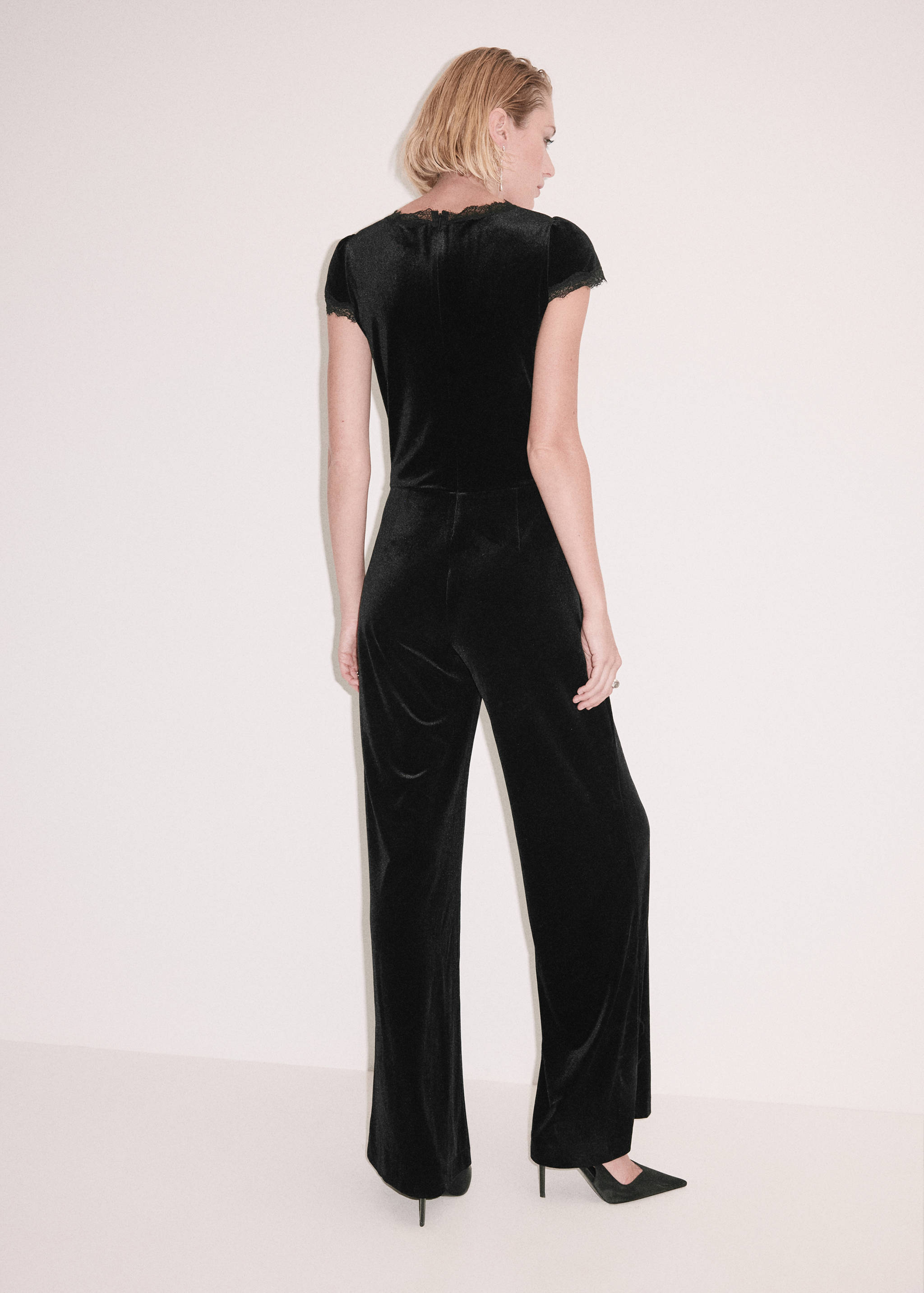 Black velvet jumpsuit with lace trim, short sleeves and straight legs, back view.