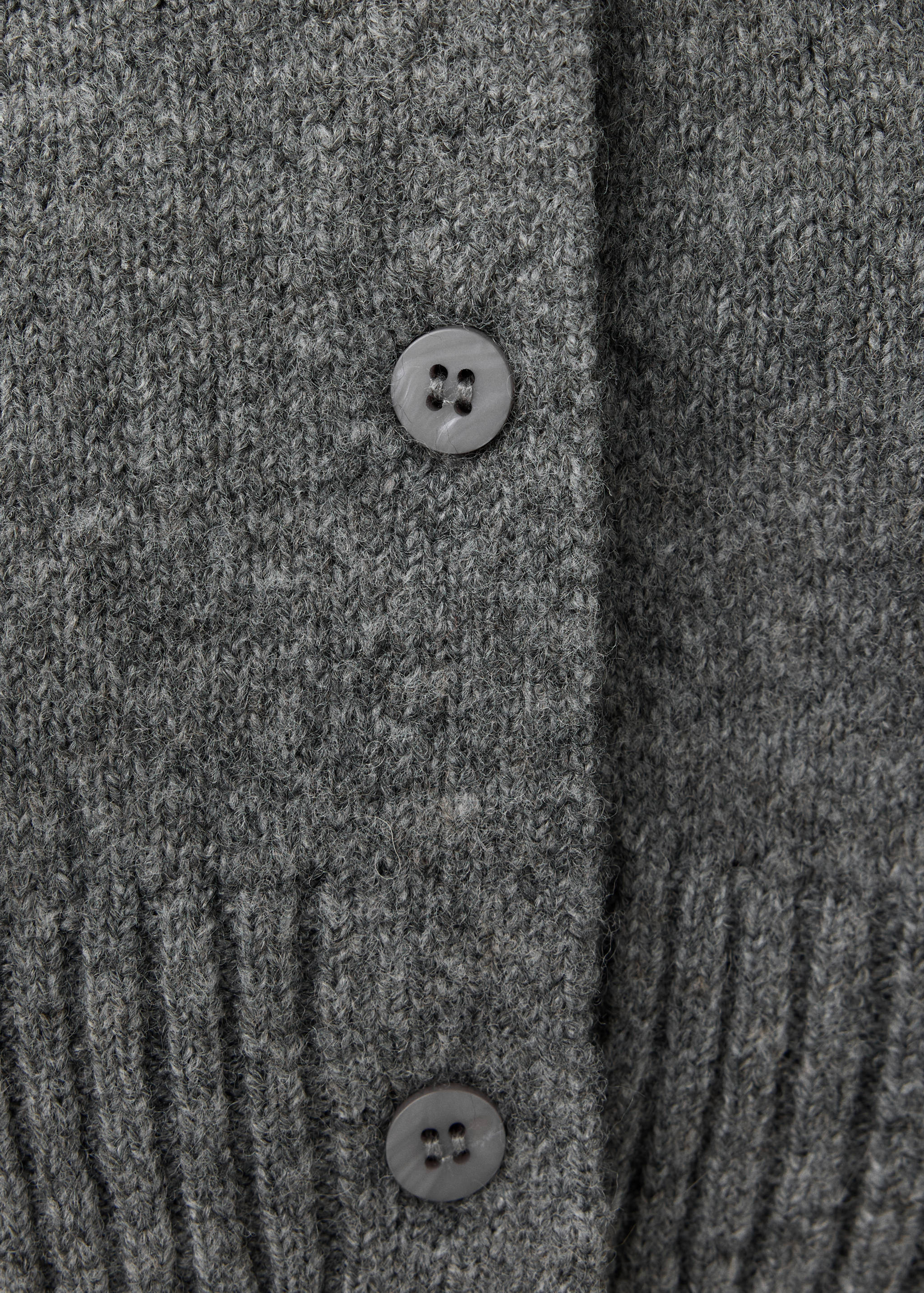 Close-up of a grey knitted cardigan showing fabric texture and buttons.
