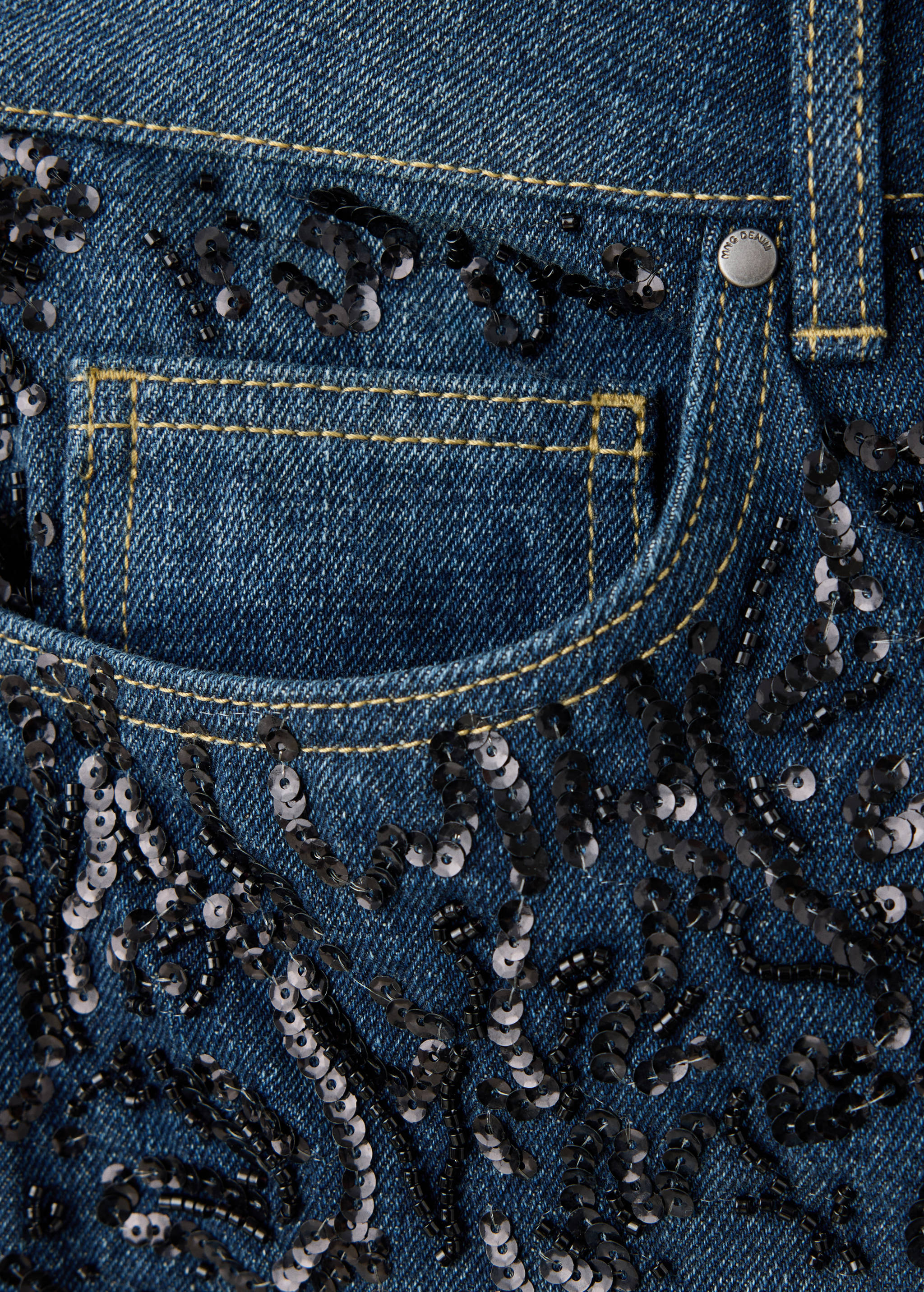 Close-up of dark blue denim jeans embellished with black sequins.