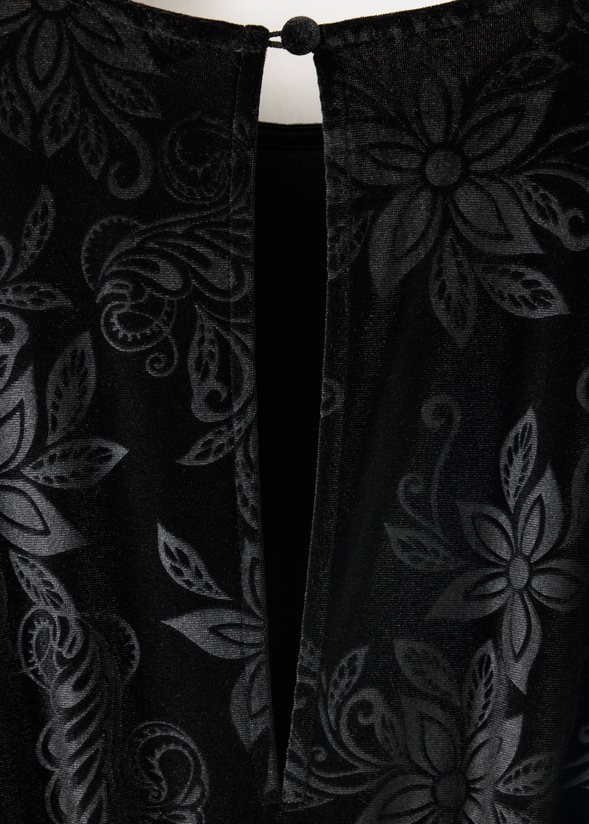 Close-up of black velvet jumpsuit fabric with tonal floral burnout pattern.
