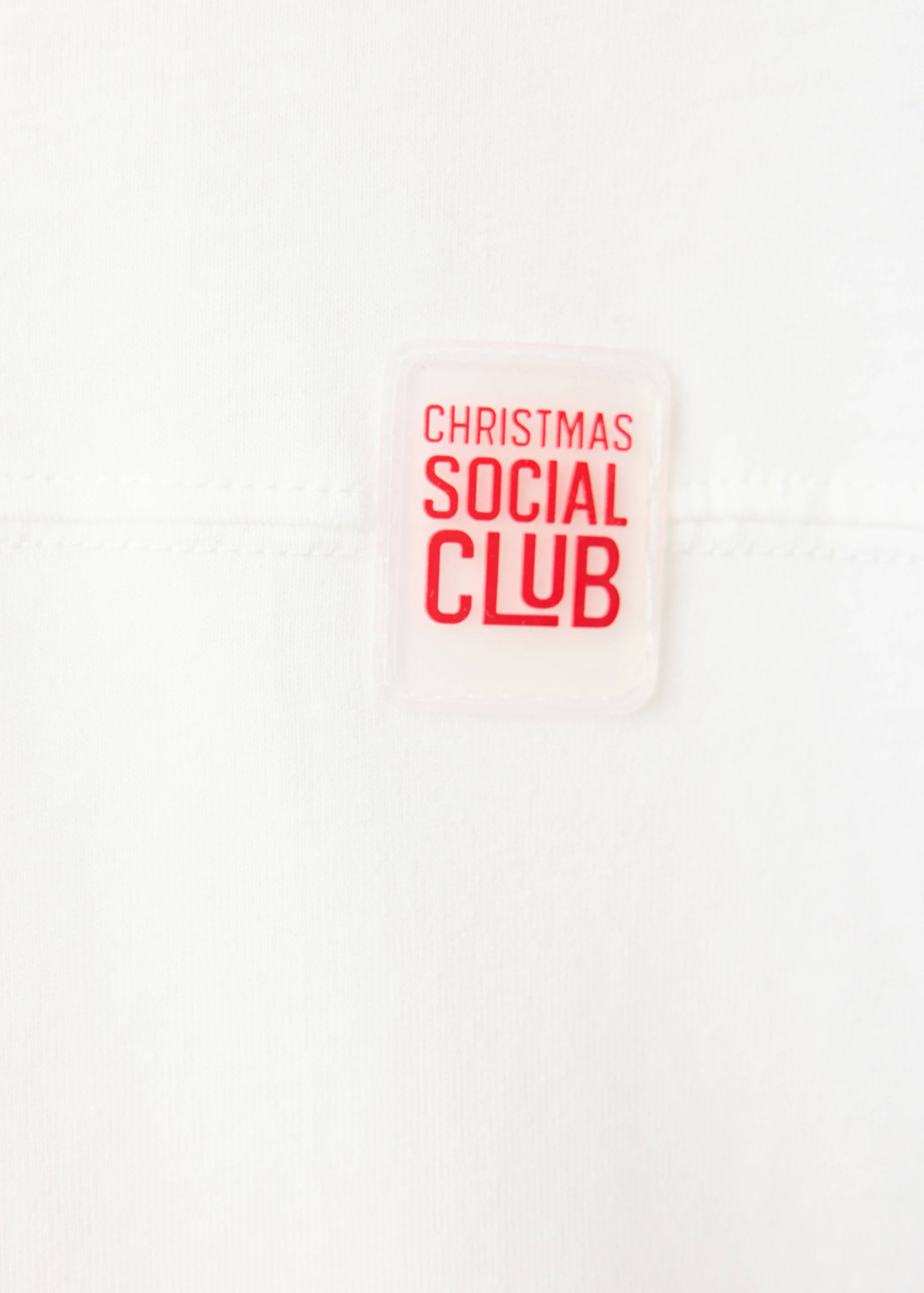 Close-up of a white t-shirt with a red Christmas Social Club text patch.