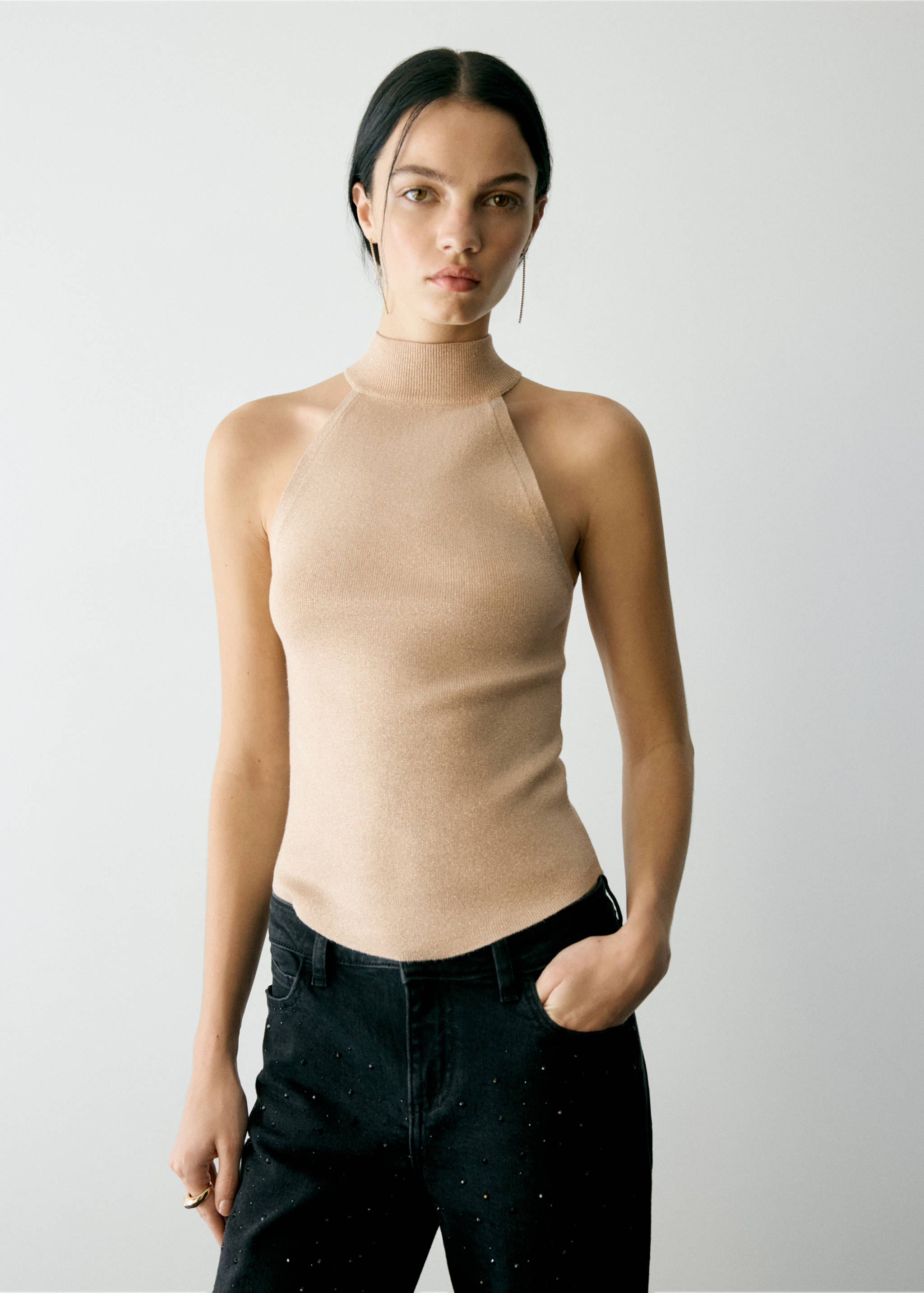 Top de punto halter en color beige de cuello alto, diseño sin mangas con sisas pronunciadas y bajo curvo.