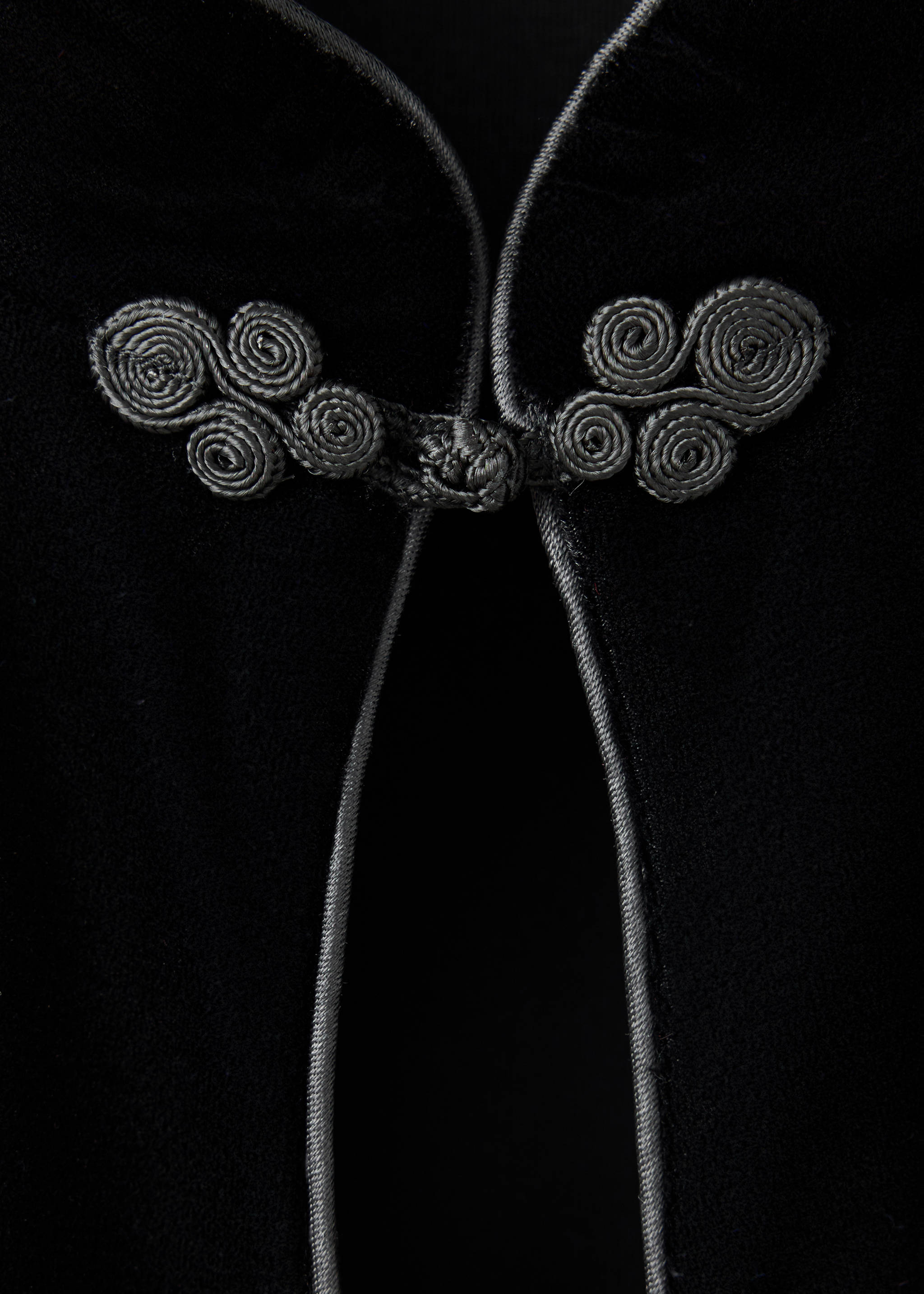 Black dress detail featuring decorative knotted frog closures.