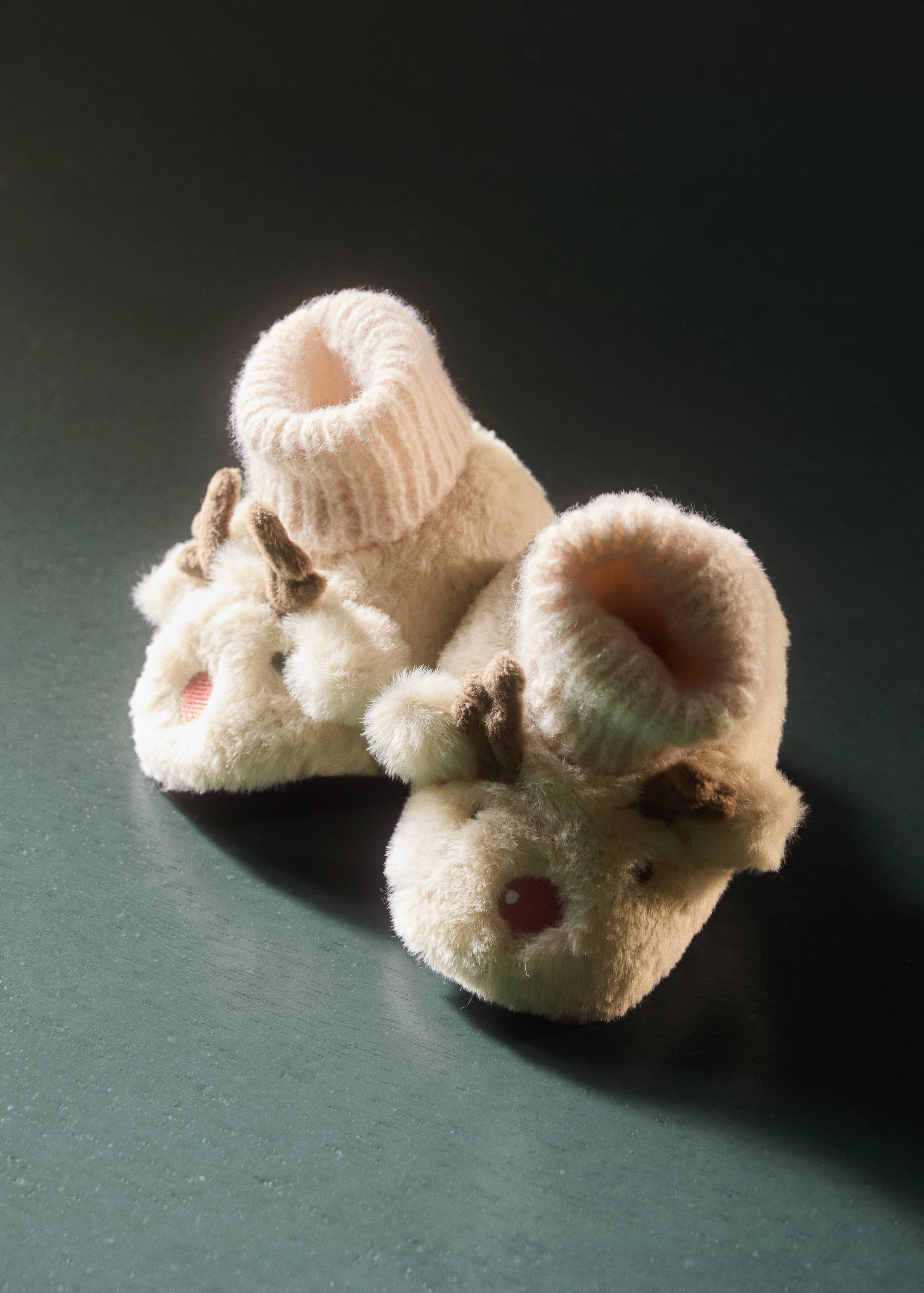 Off-white plush faux-fur home slippers with reindeer details and a ribbed knit collar.