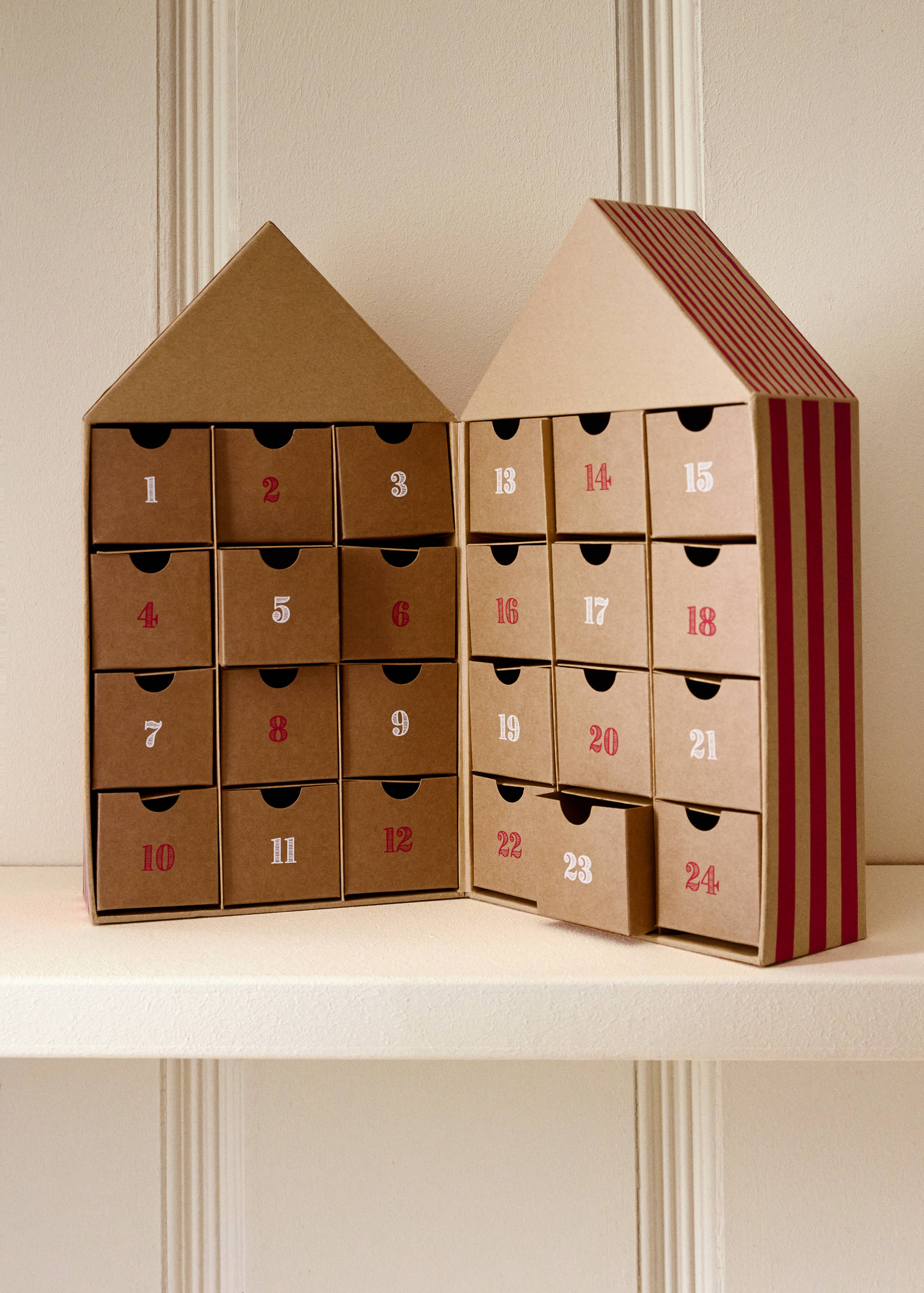 House-shaped cardboard advent calendar with numbered drawers and red stripes.