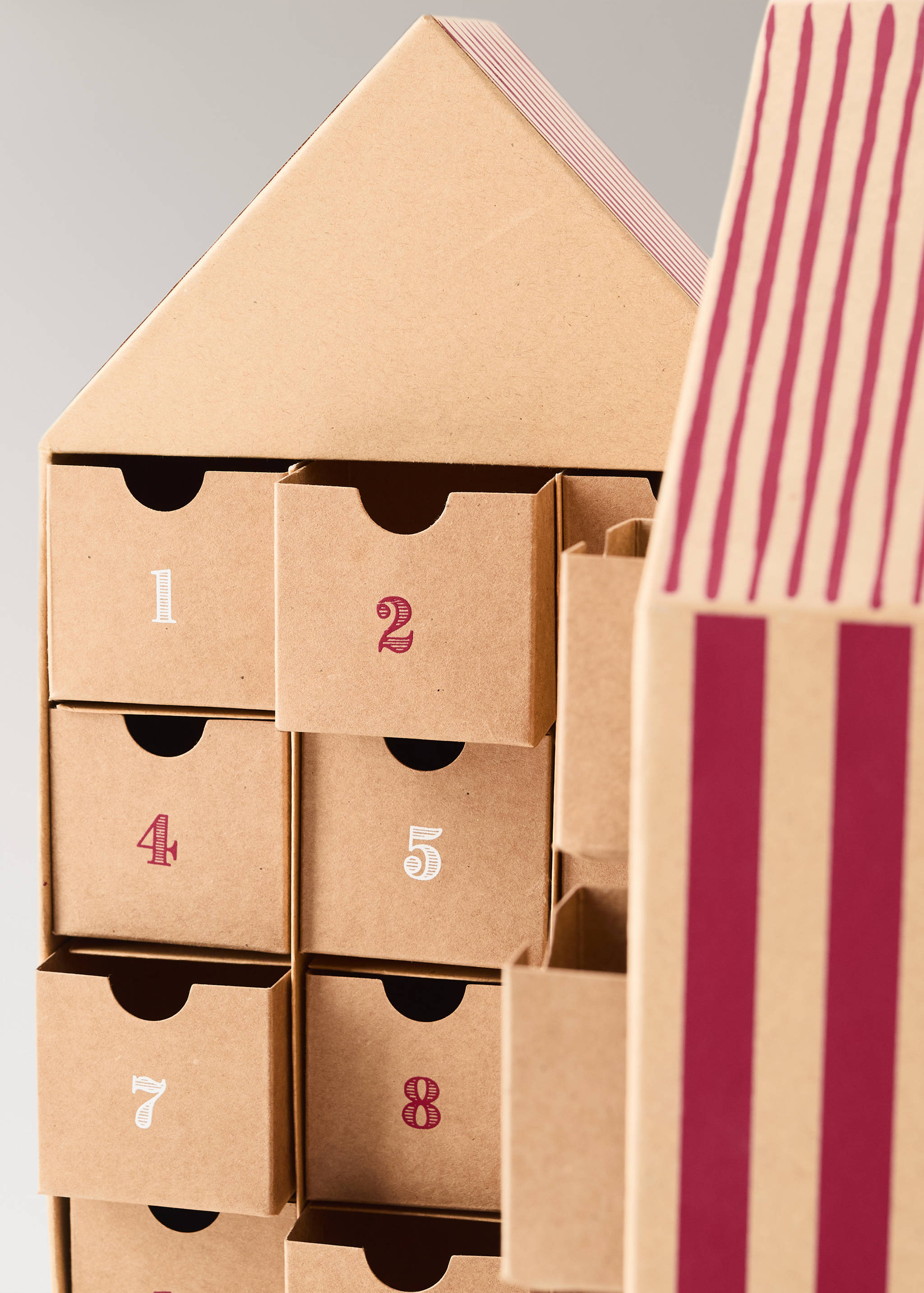 Close-up of a house-shaped brown cardboard advent calendar with numbered drawers and striped roof detail.