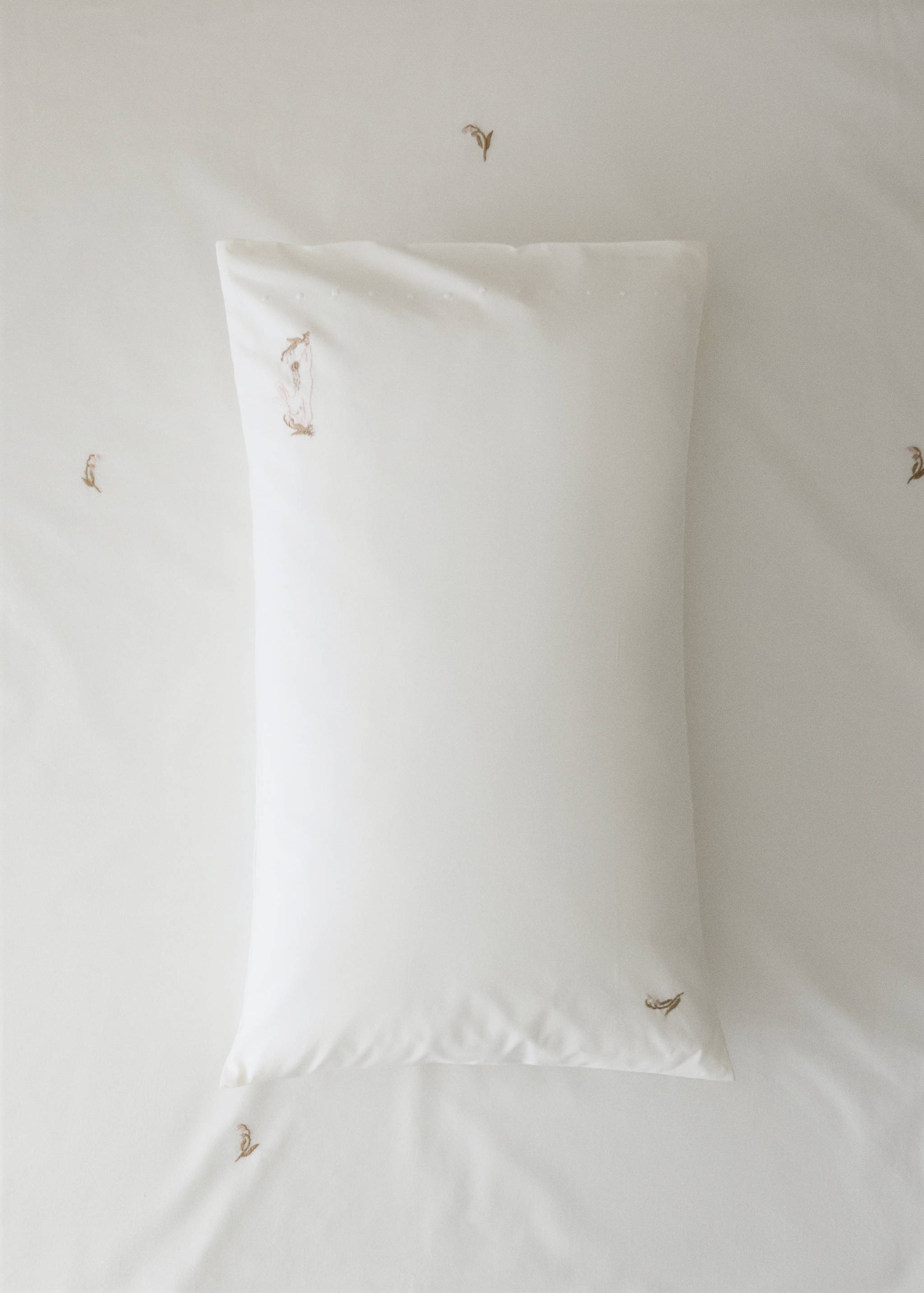 White crib pillowcase with delicate brown embroidery.